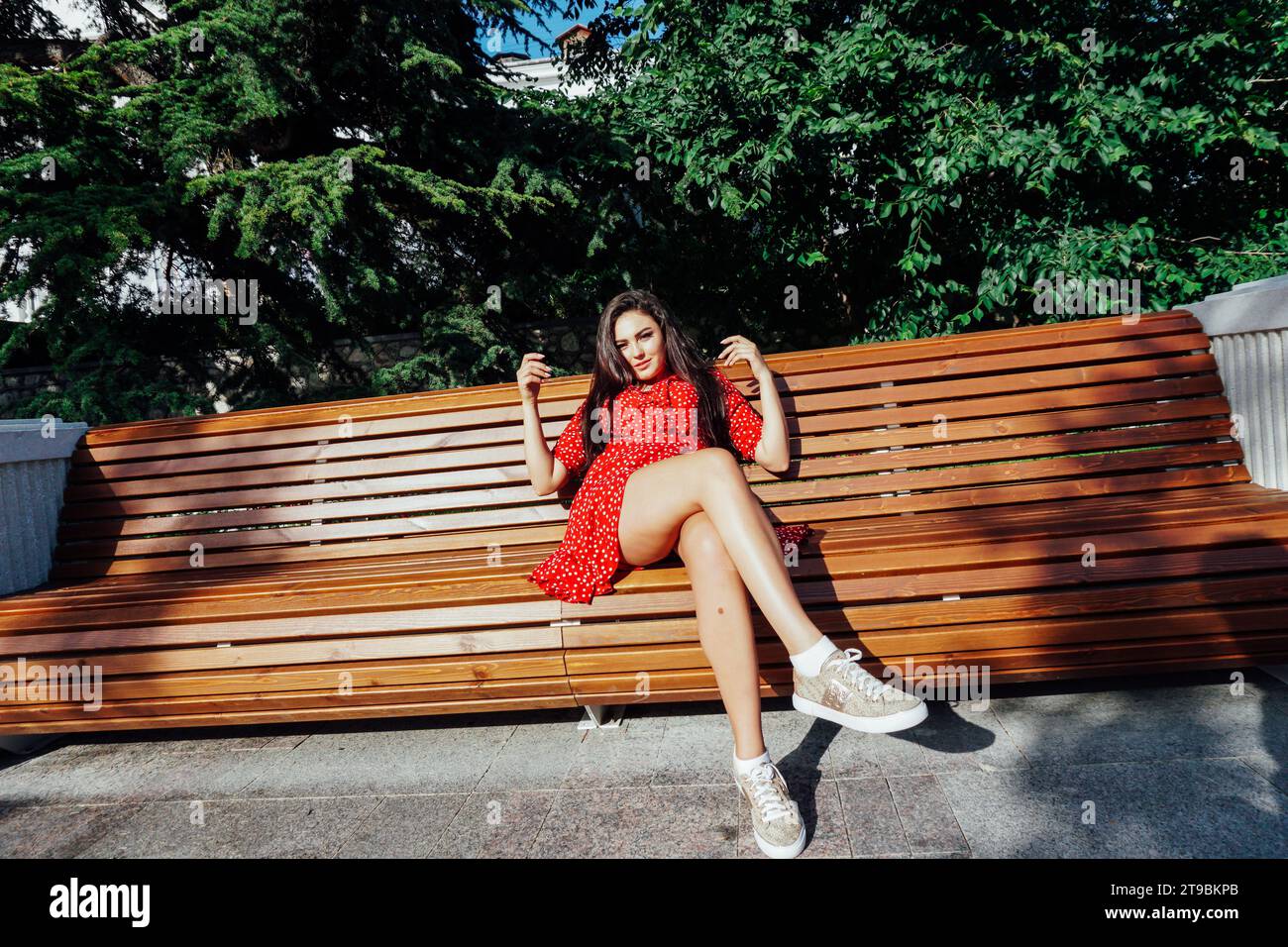 Brunette woman in red dress sitting on a bench for a walk Stock Photo ...