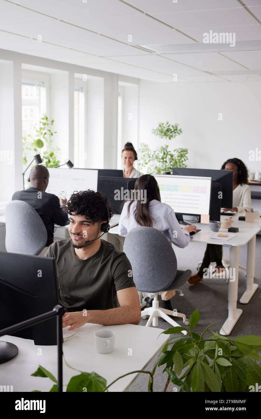 Man wearing headset using desktop PC in office Stock Photo
