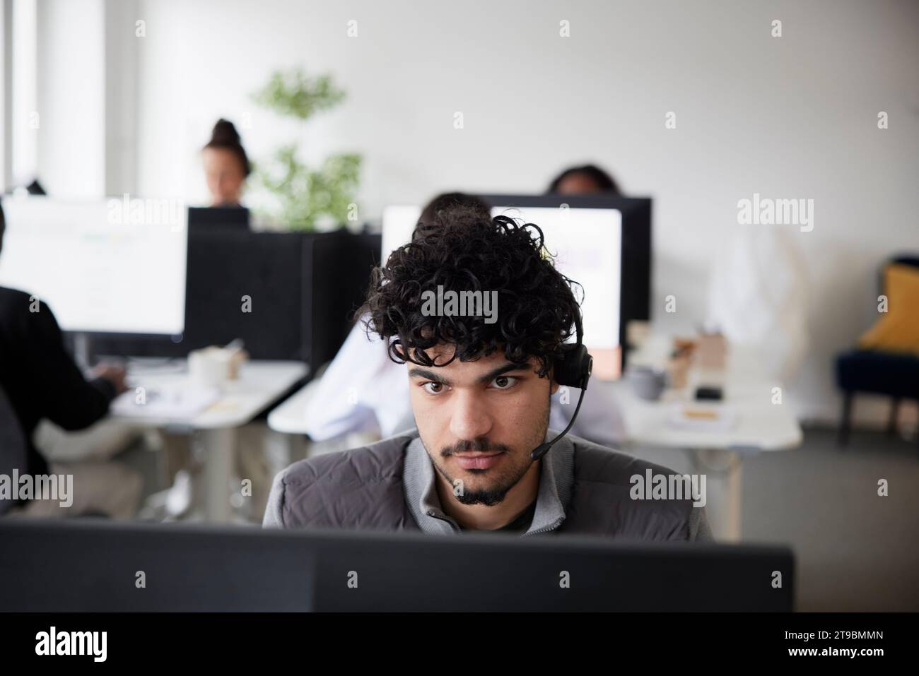 Man wearing headset using desktop PC in office Stock Photo