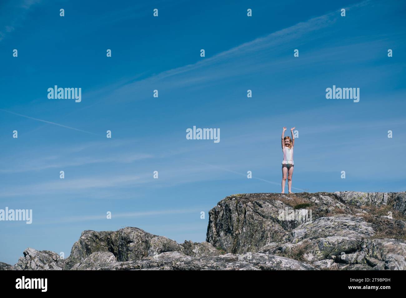 Girl standing on rock formation against blue sky on sunny day Stock Photo
