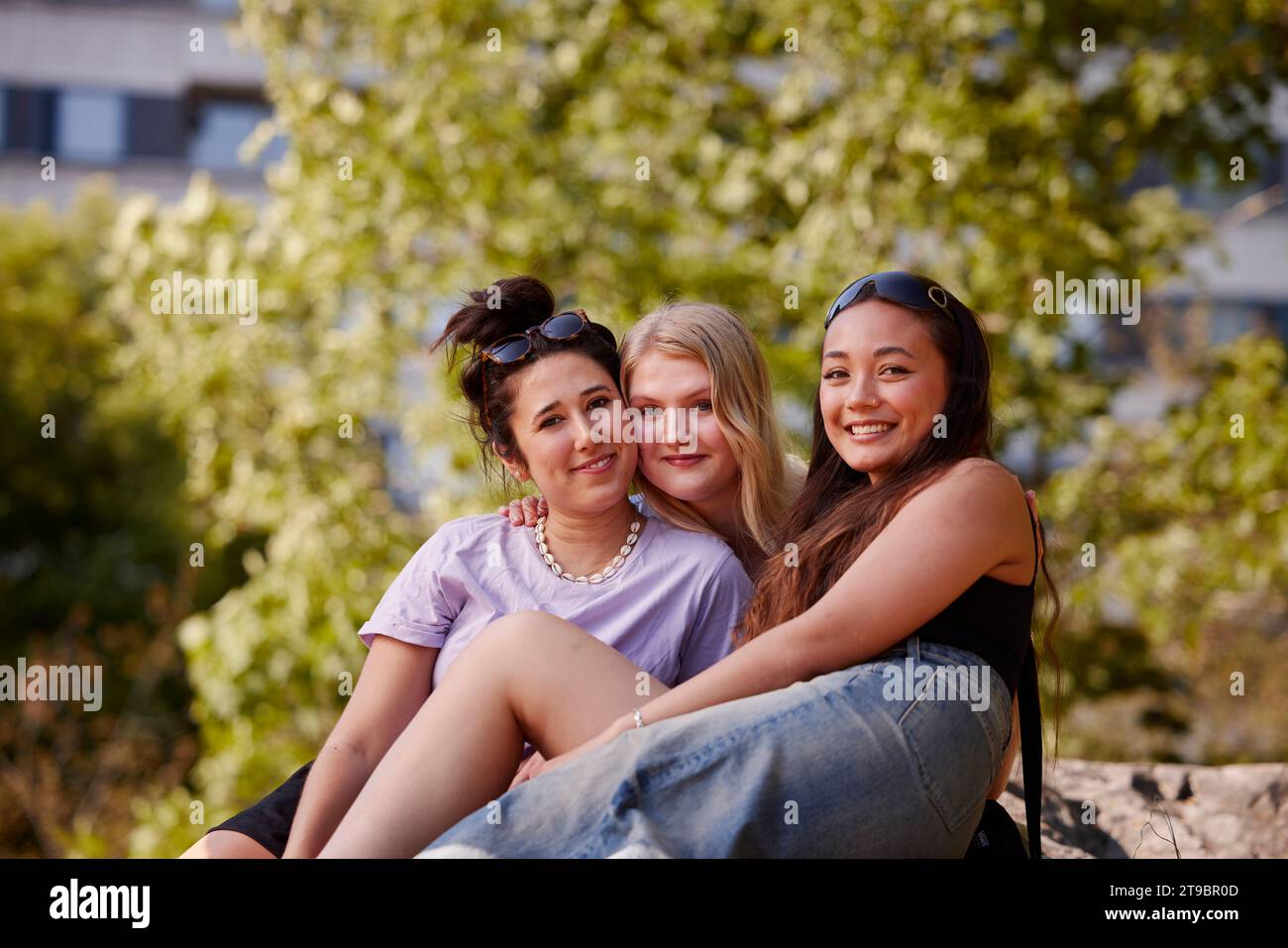 Three young female friends sitting together and looking at camera Stock Photo