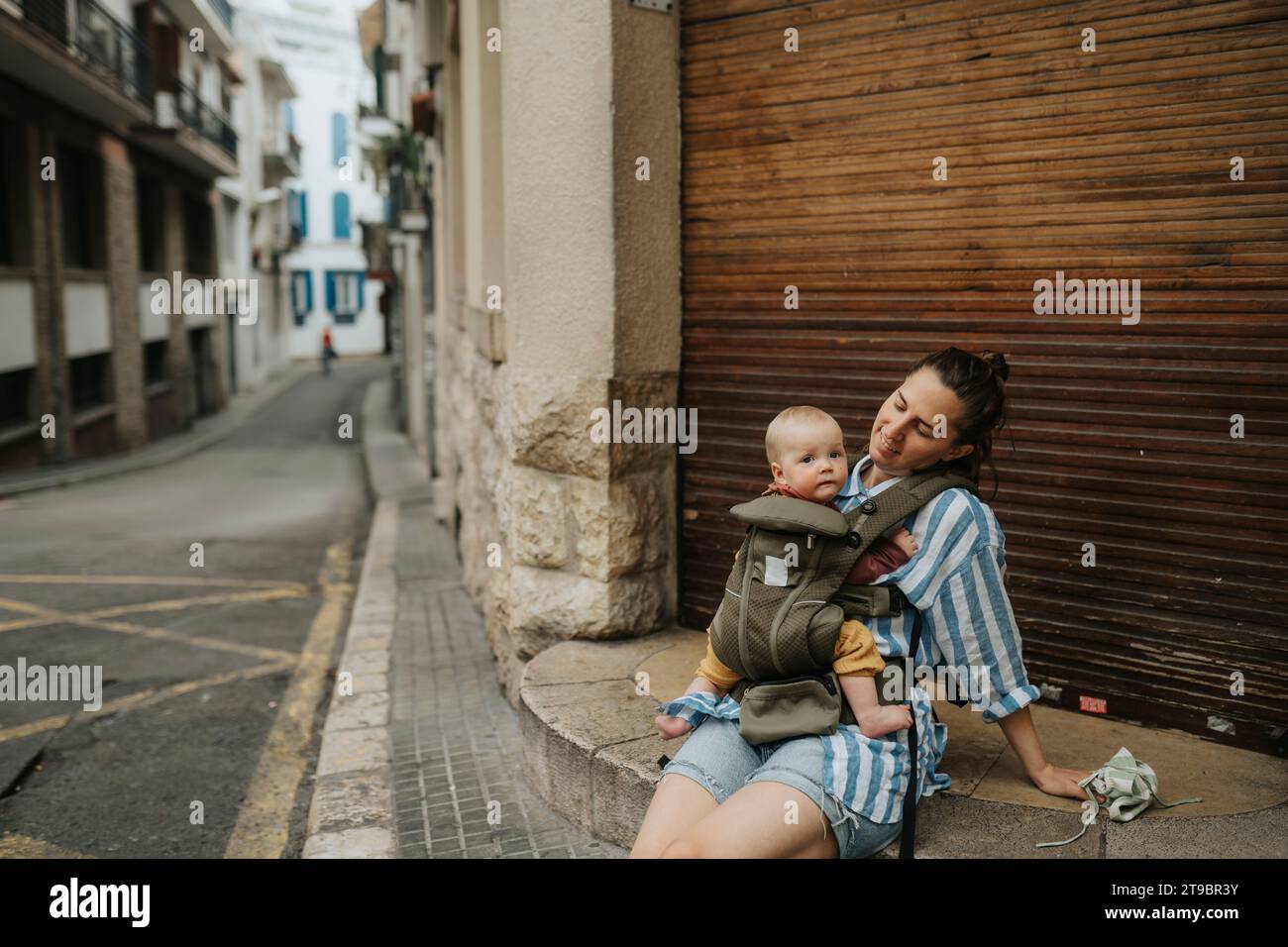 Mother with baby sitting on street Stock Photo
