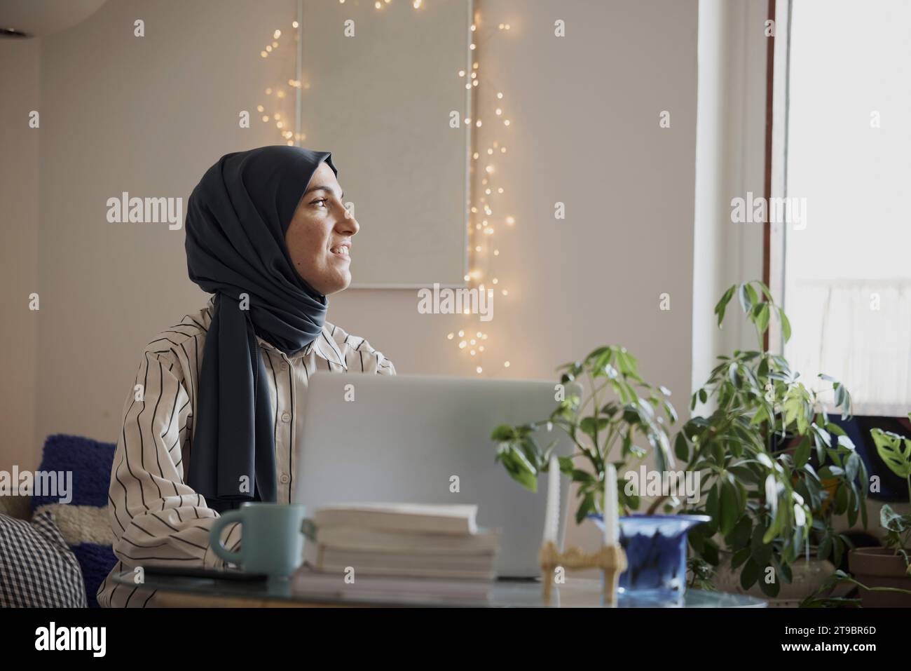 Contemplative female freelancer with laptop in living room while working from home Stock Photo