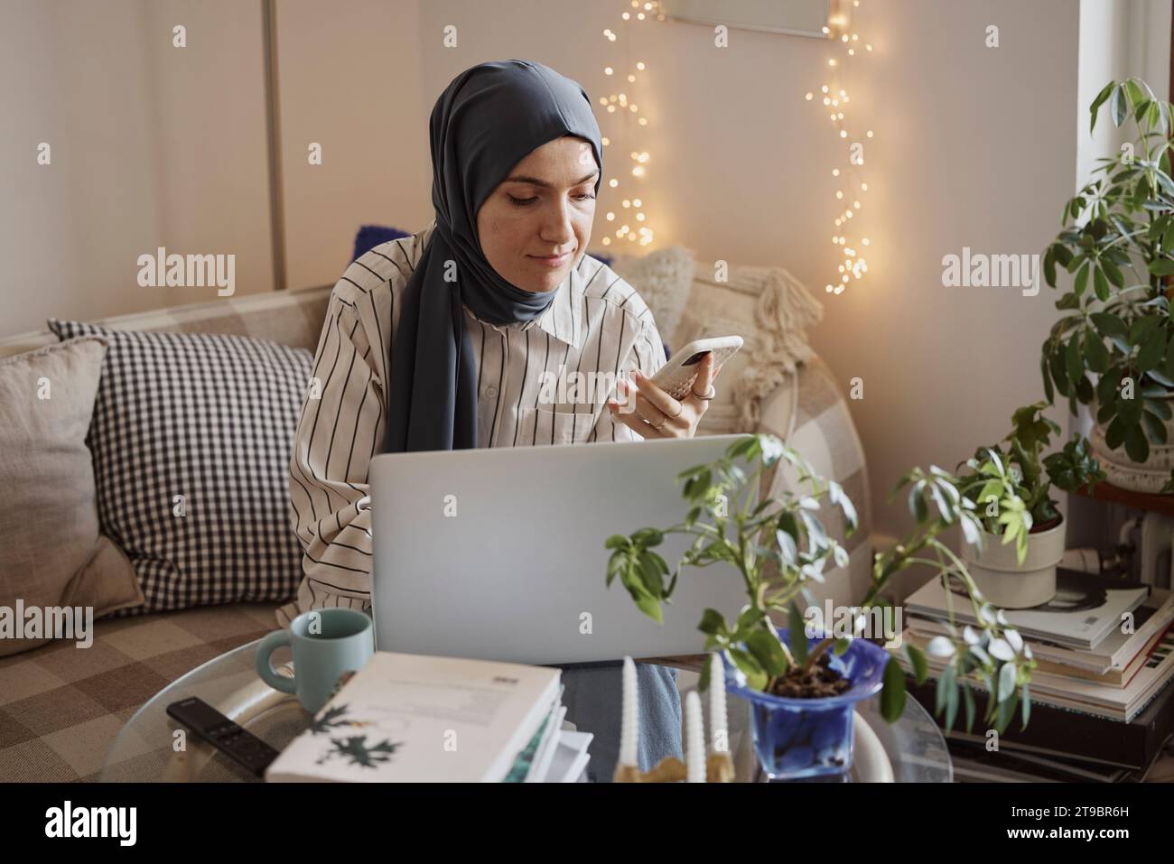Young businesswoman using smart phone by laptop while working in living room Stock Photo