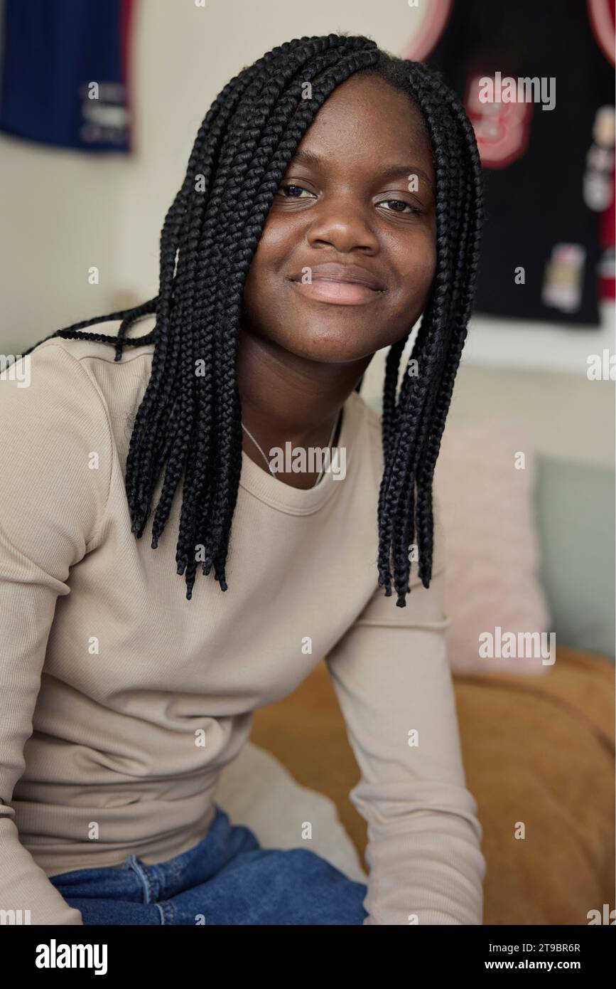 Portrait of smiling female teenager with braided hair sitting at home Stock Photo