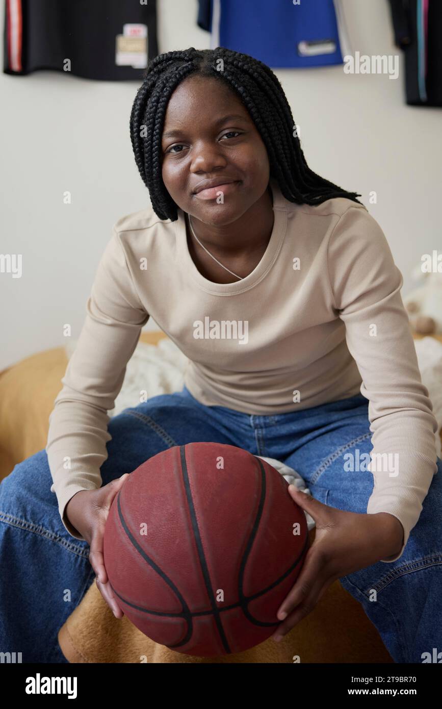 Portrait of teenage girl holding basketball while sitting in bedroom at home Stock Photo