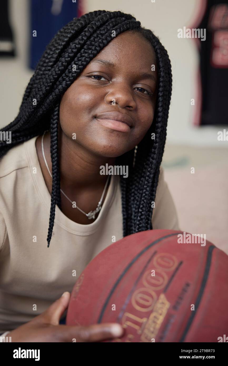Portrait of smiling female teenager holding basketball while sitting at home Stock Photo