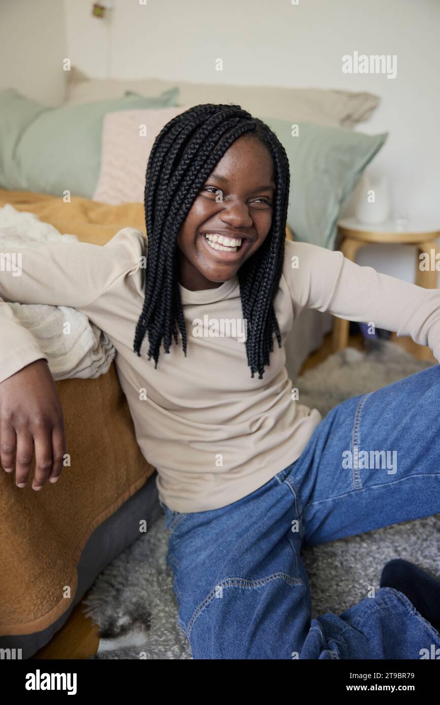 Happy teenage girl with braided hair sitting in bedroom at home Stock Photo