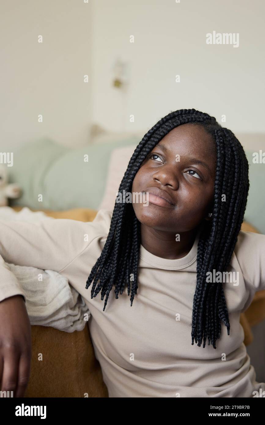 Contemplative teenage girl with braided hair sitting at home Stock Photo