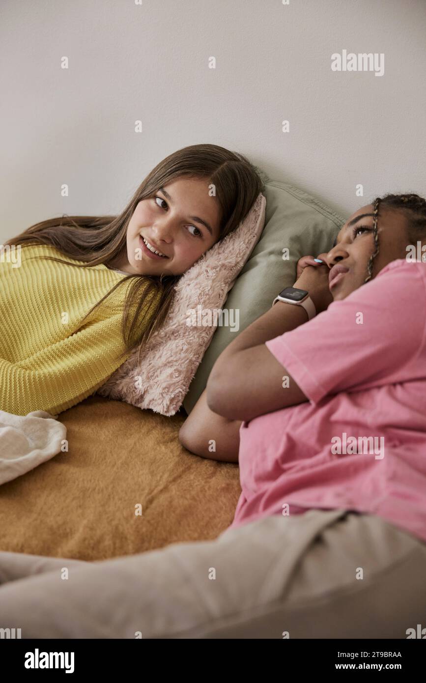 Multiracial female friends lying in bed while resting at home Stock Photo