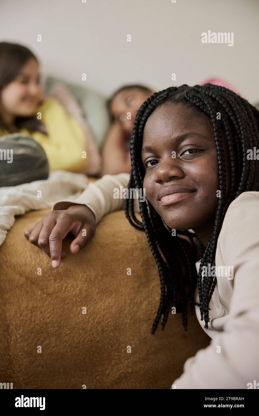 Smiling teenage girl with braided hair by female friends lying in bedroom Stock Photo