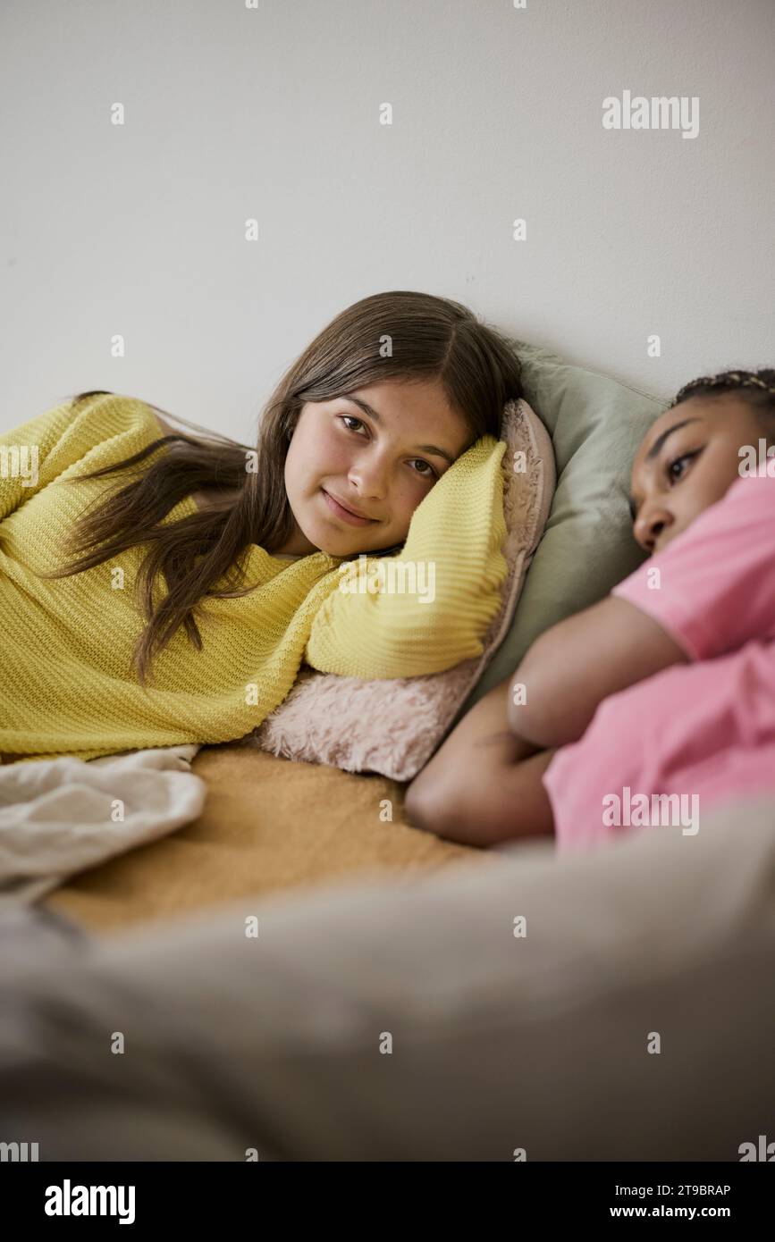 Teenage girl resting on bed with female friend in bedroom at home Stock Photo