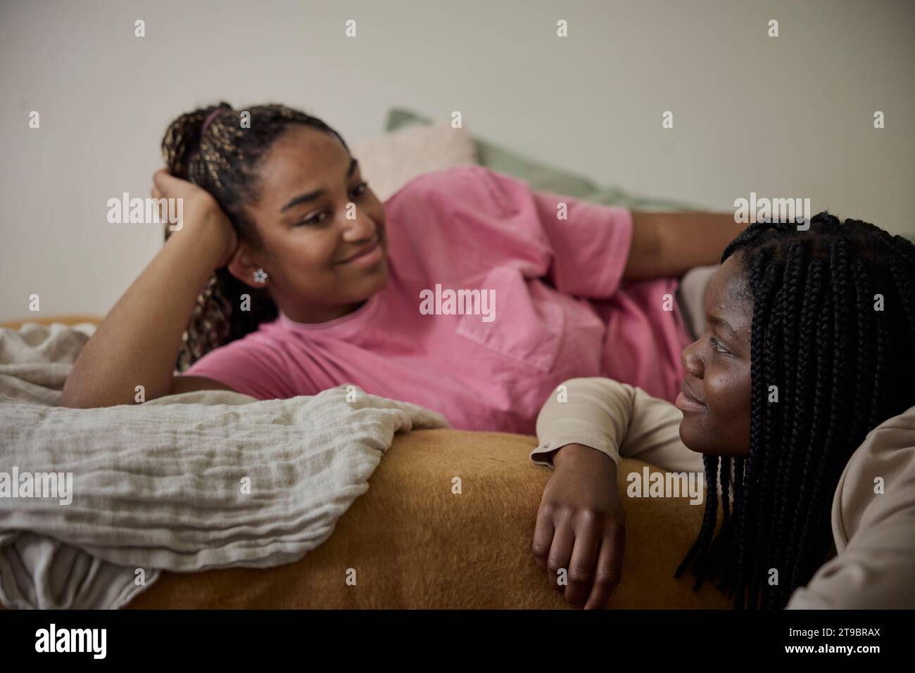 Teenage girl talking with female friend lying on bed in bedroom Stock Photo