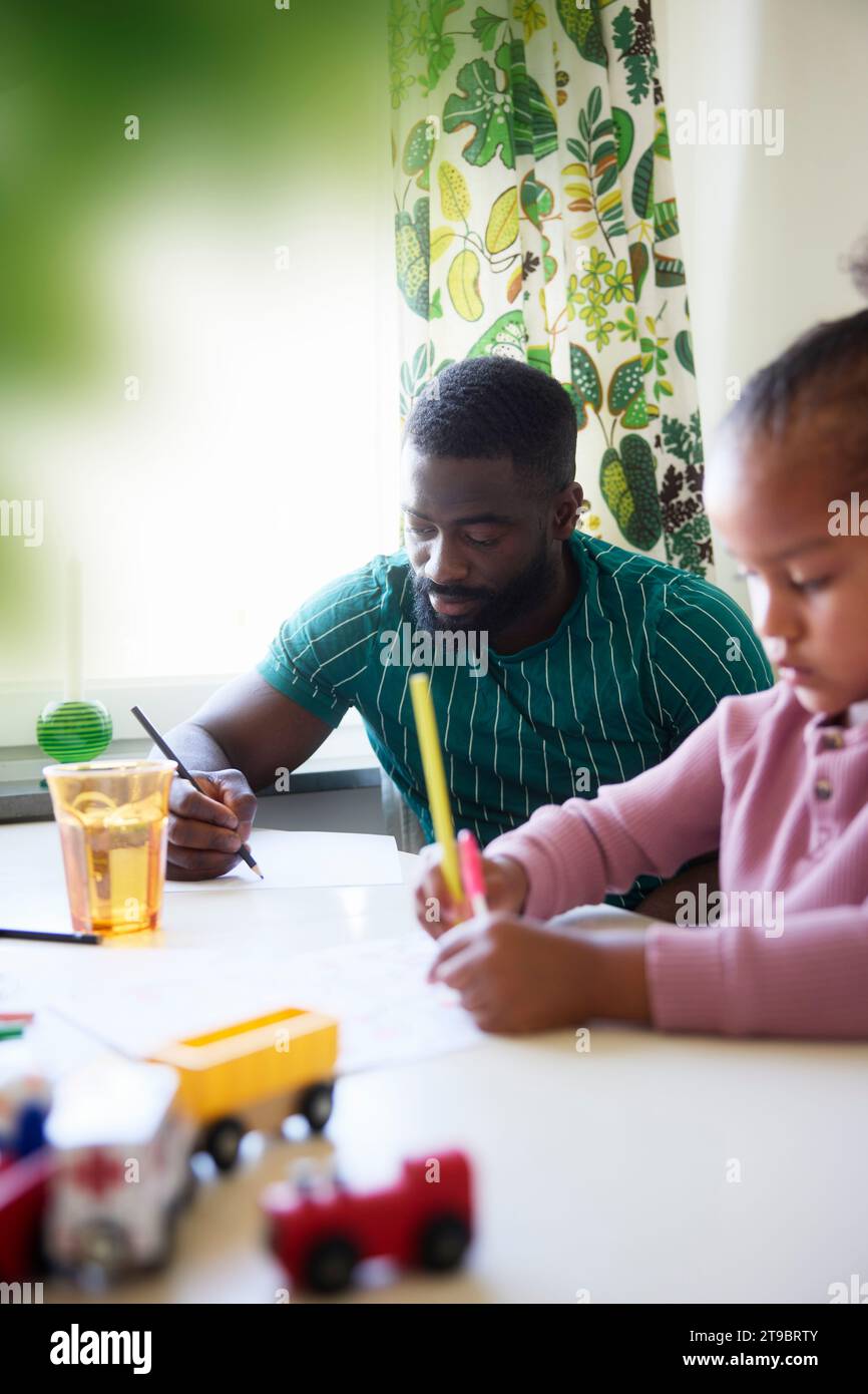Father and daughter drawing while sitting at dining table Stock Photo