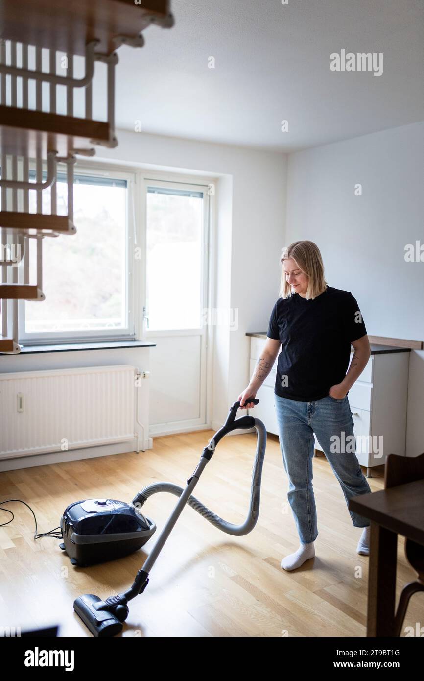 Full length of young woman using vacuum cleaner on hardwood floor at home Stock Photo