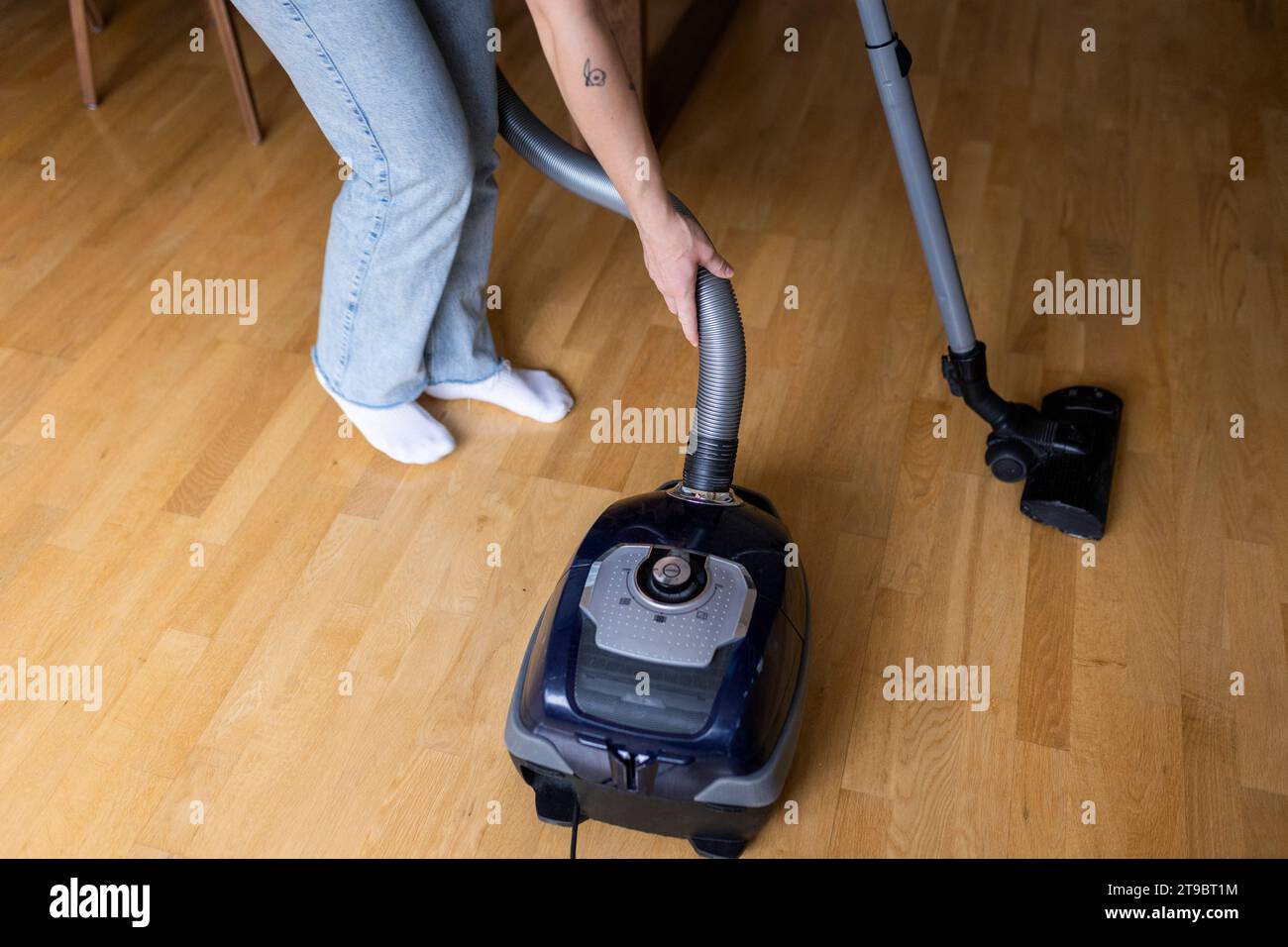 Low section of young woman using vacuum cleaner on hardwood floor at home Stock Photo