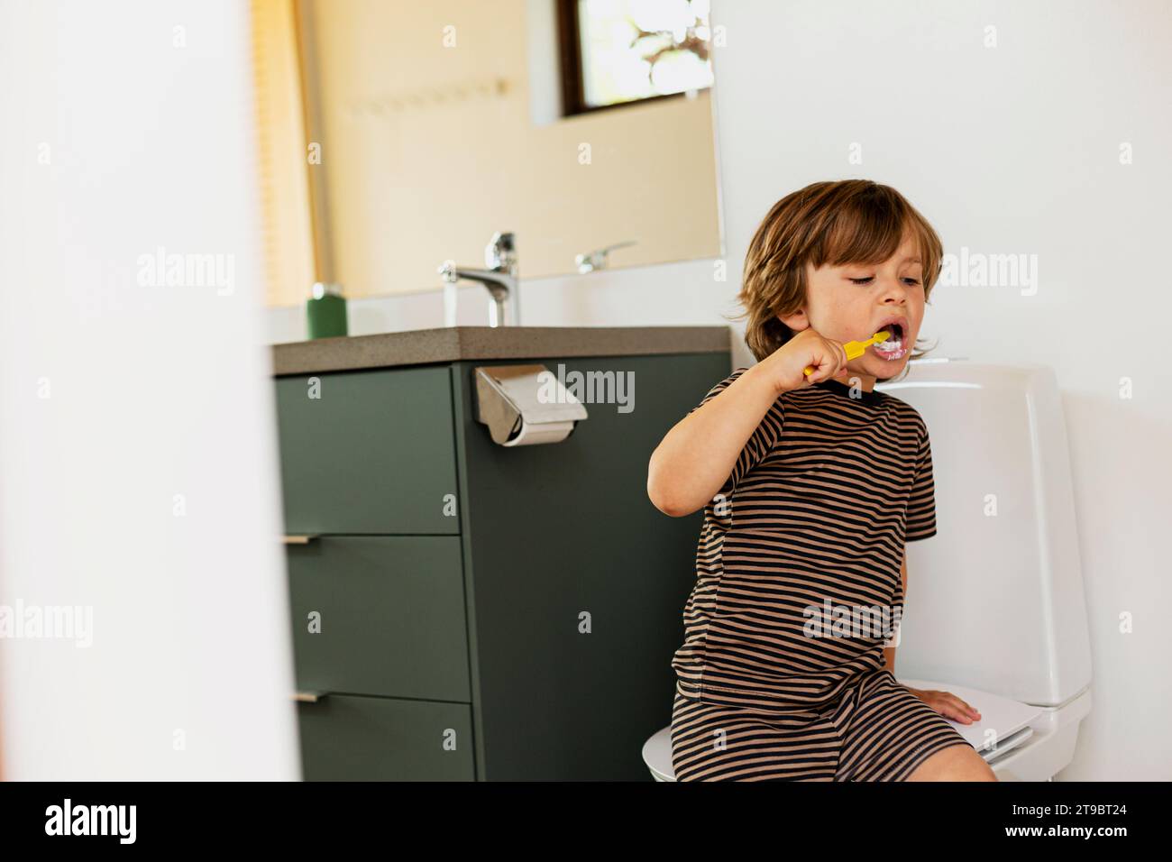 Boy brushing while sitting in bathroom Stock Photo