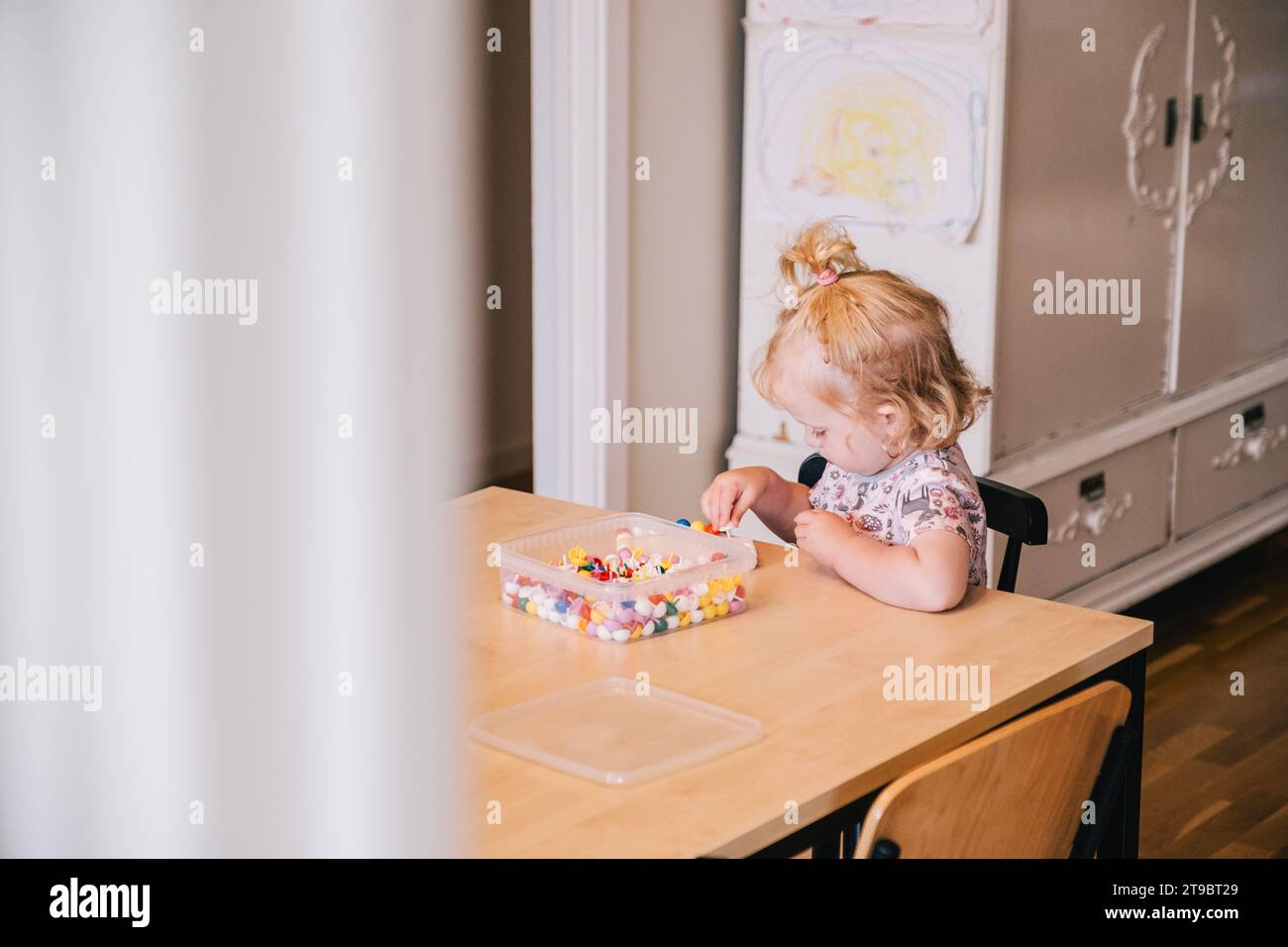 Blond girl playing with beads on table at home Stock Photo