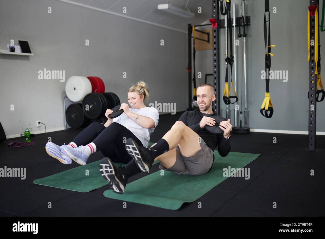 Full length of happy mid adult couple exercising with weights at health club Stock Photo