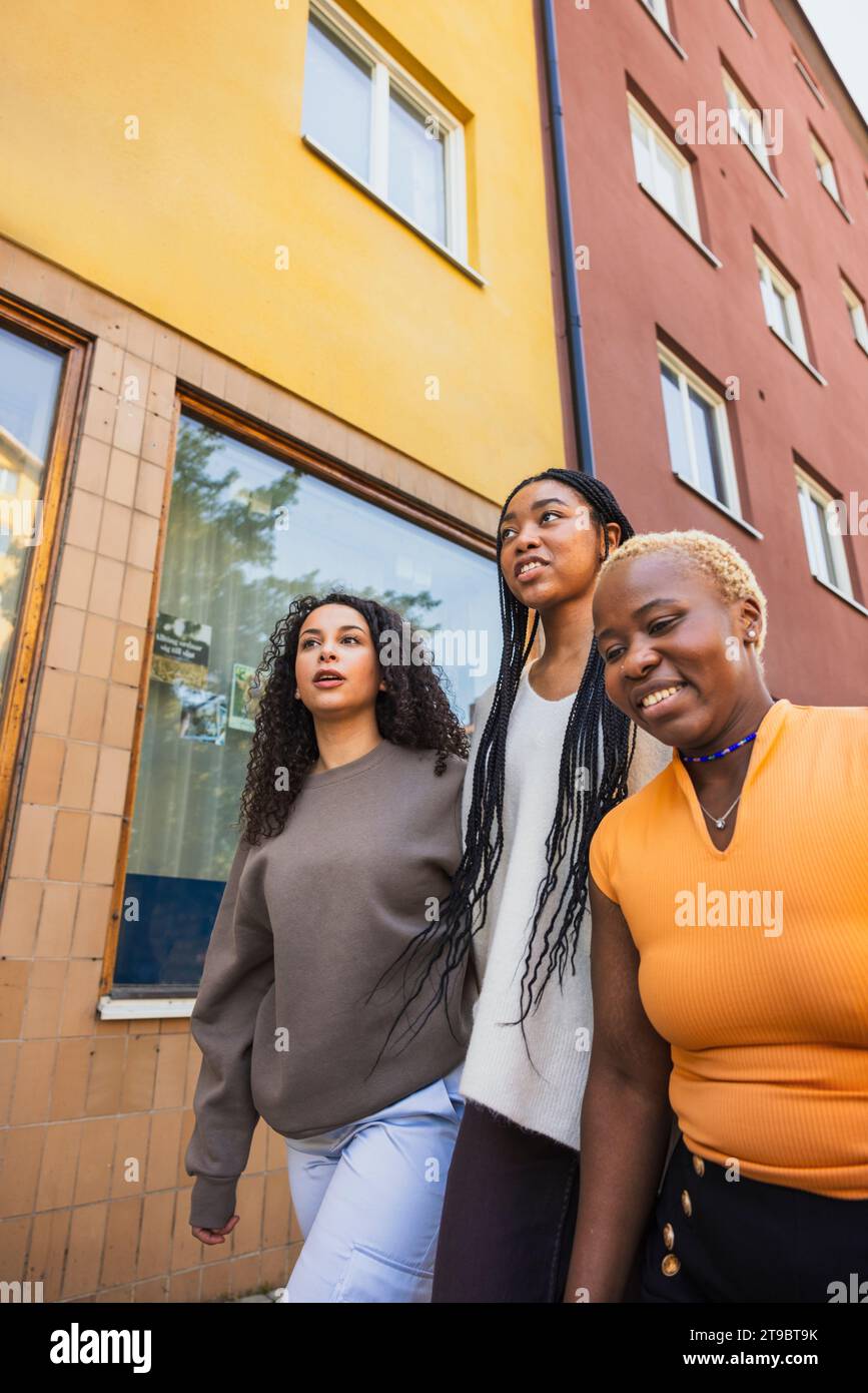 Multiracial female friends walking by building while hanging out on weekend Stock Photo