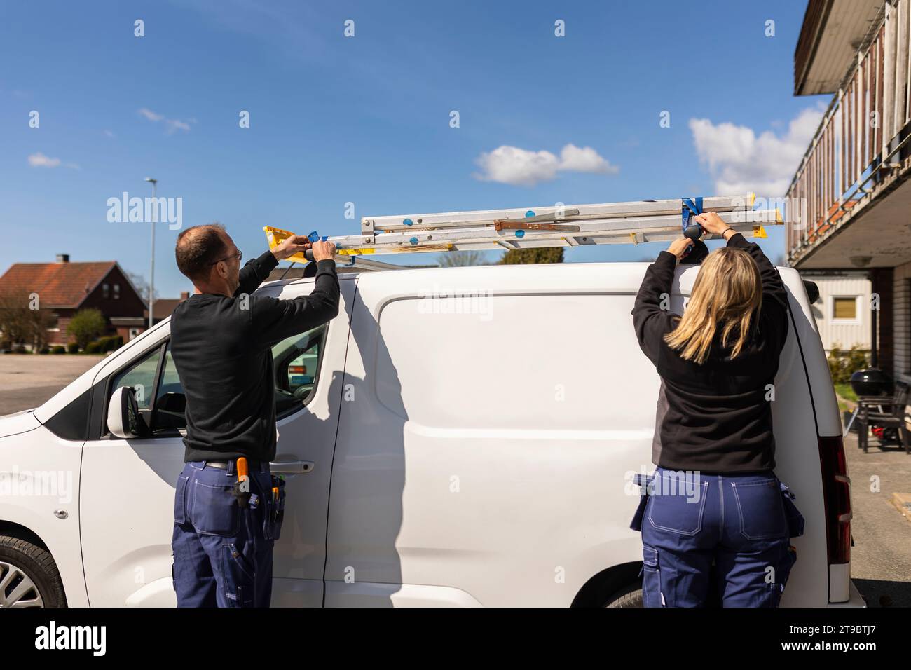 Rear view of male and female electricians getting ladder from van on sunny day Stock Photo