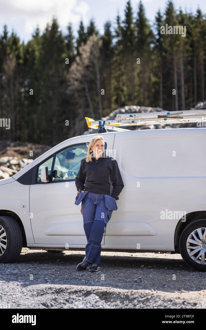 Female technician with legs crossed at ankle and leaning on van during sunny day Stock Photo