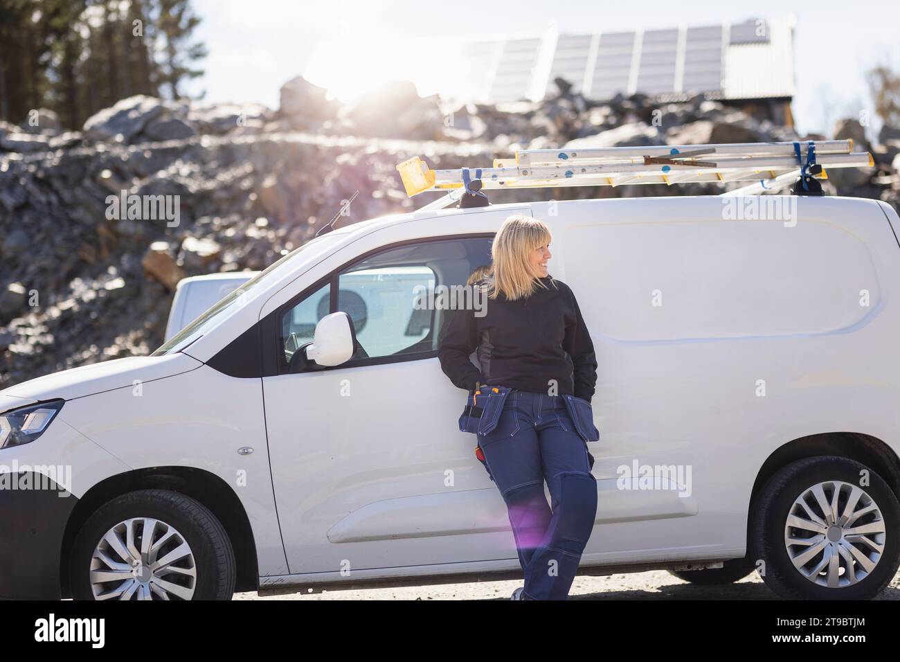 Female electrician leaning on van during sunny day Stock Photo