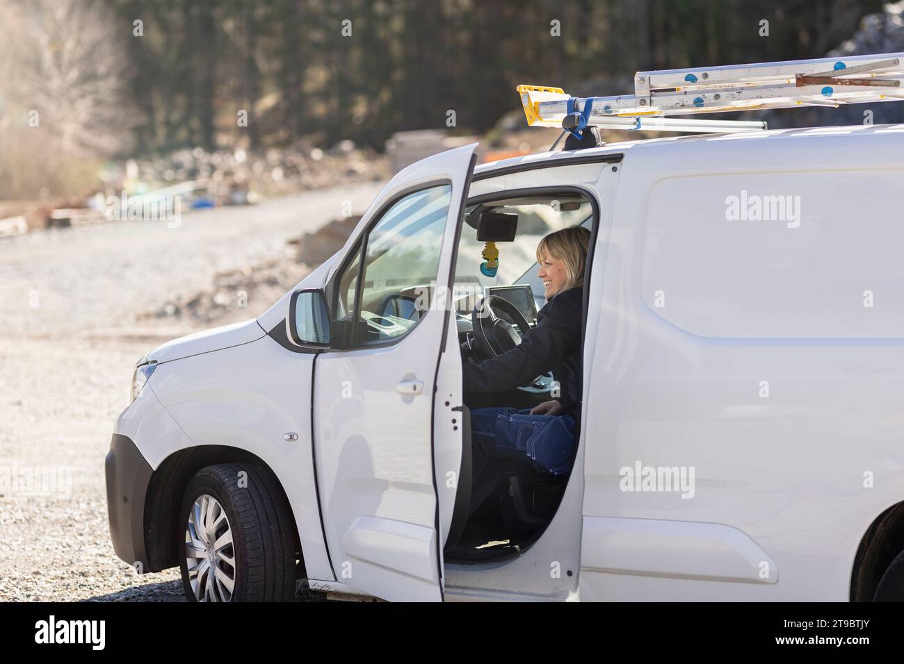 Smiling female technician sitting in van on sunny day Stock Photo