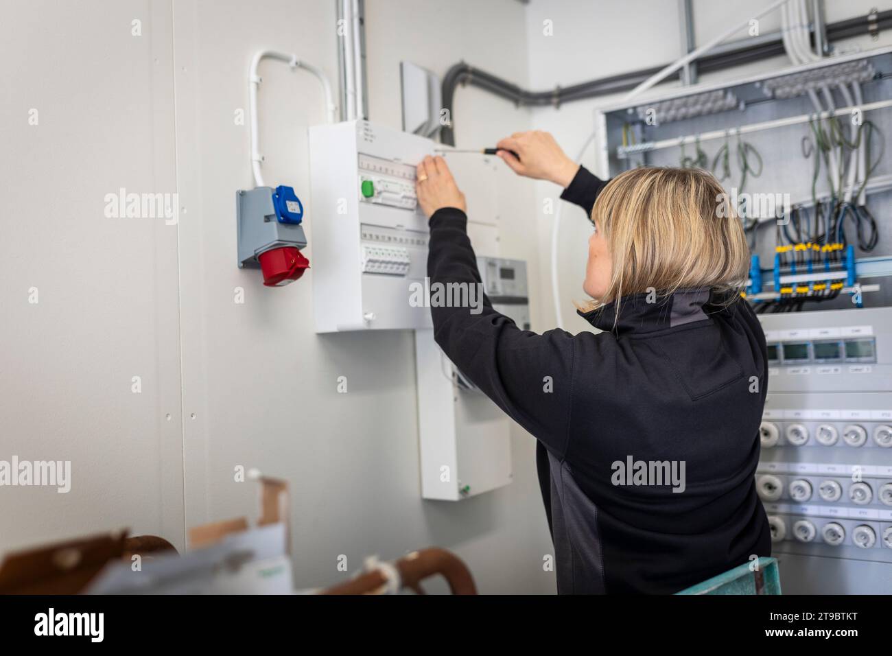 Blond female technician installing fuse box while working in control room of industry Stock Photo