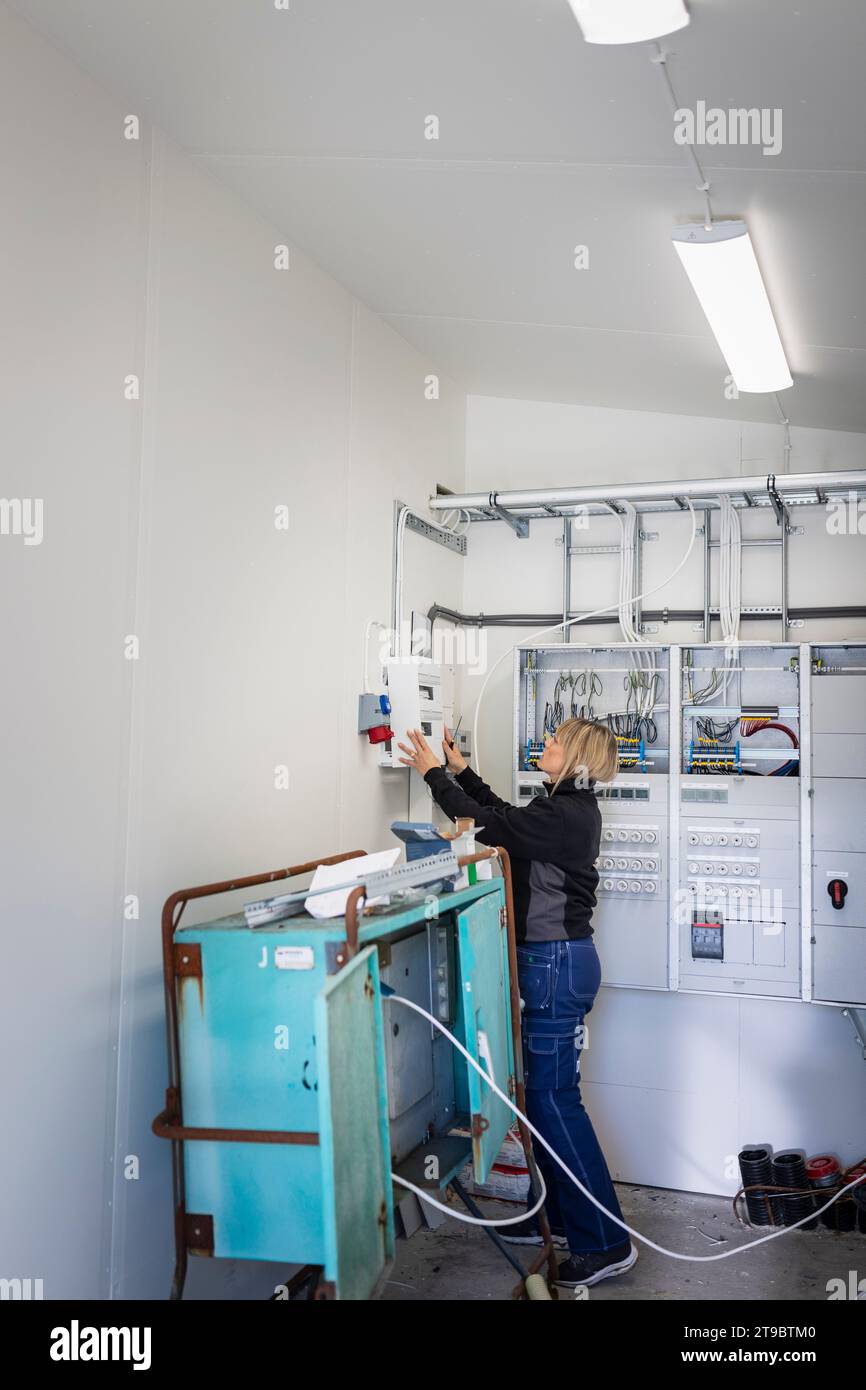 Female electrician installing fuse box while standing in control room at industry Stock Photo