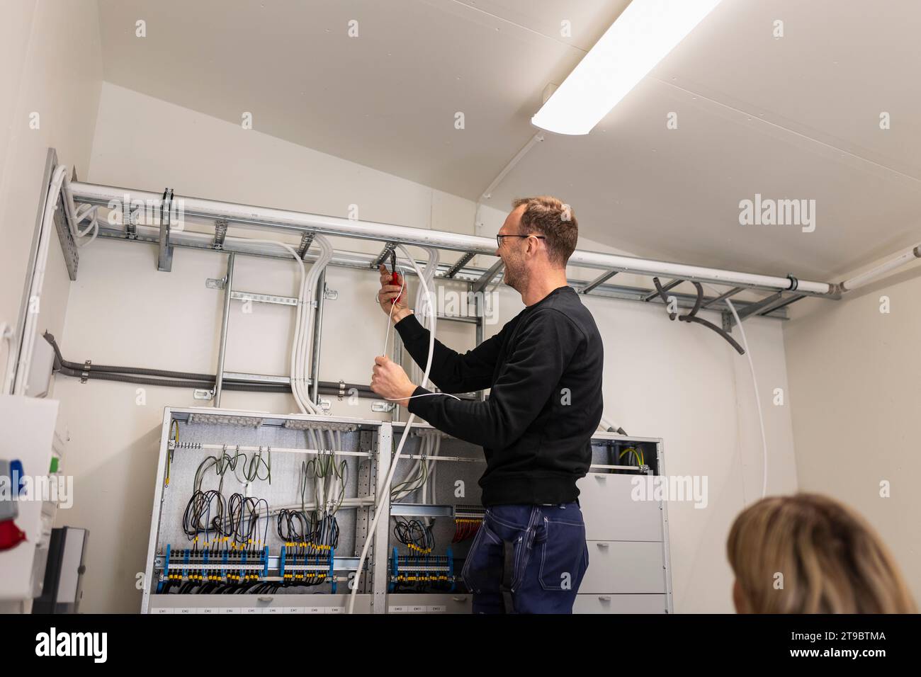 Male technician fixing cable wires on ladder in meter room Stock Photo