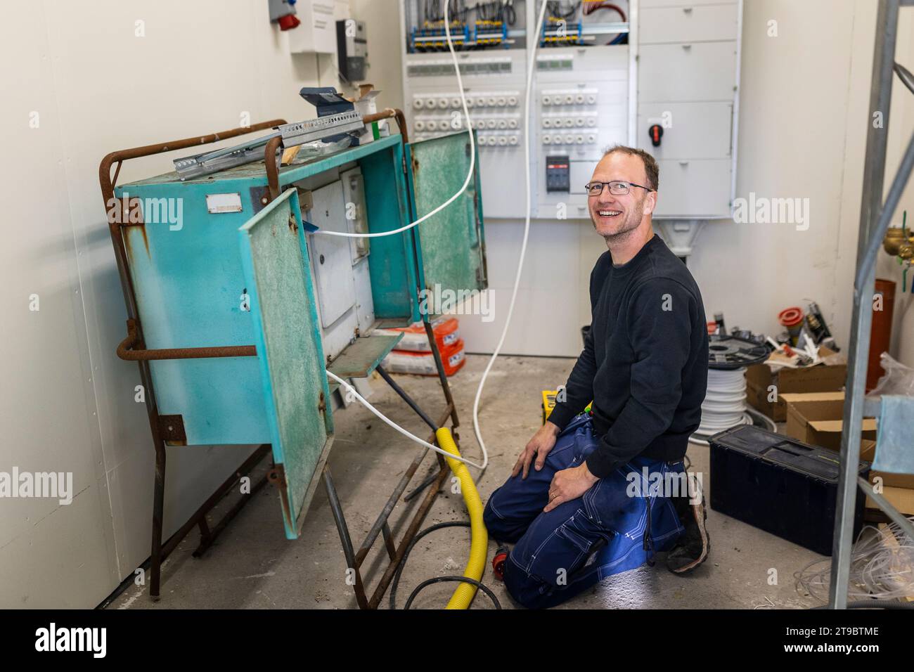 Smiling male electrician kneeling by electric panel in industry Stock Photo
