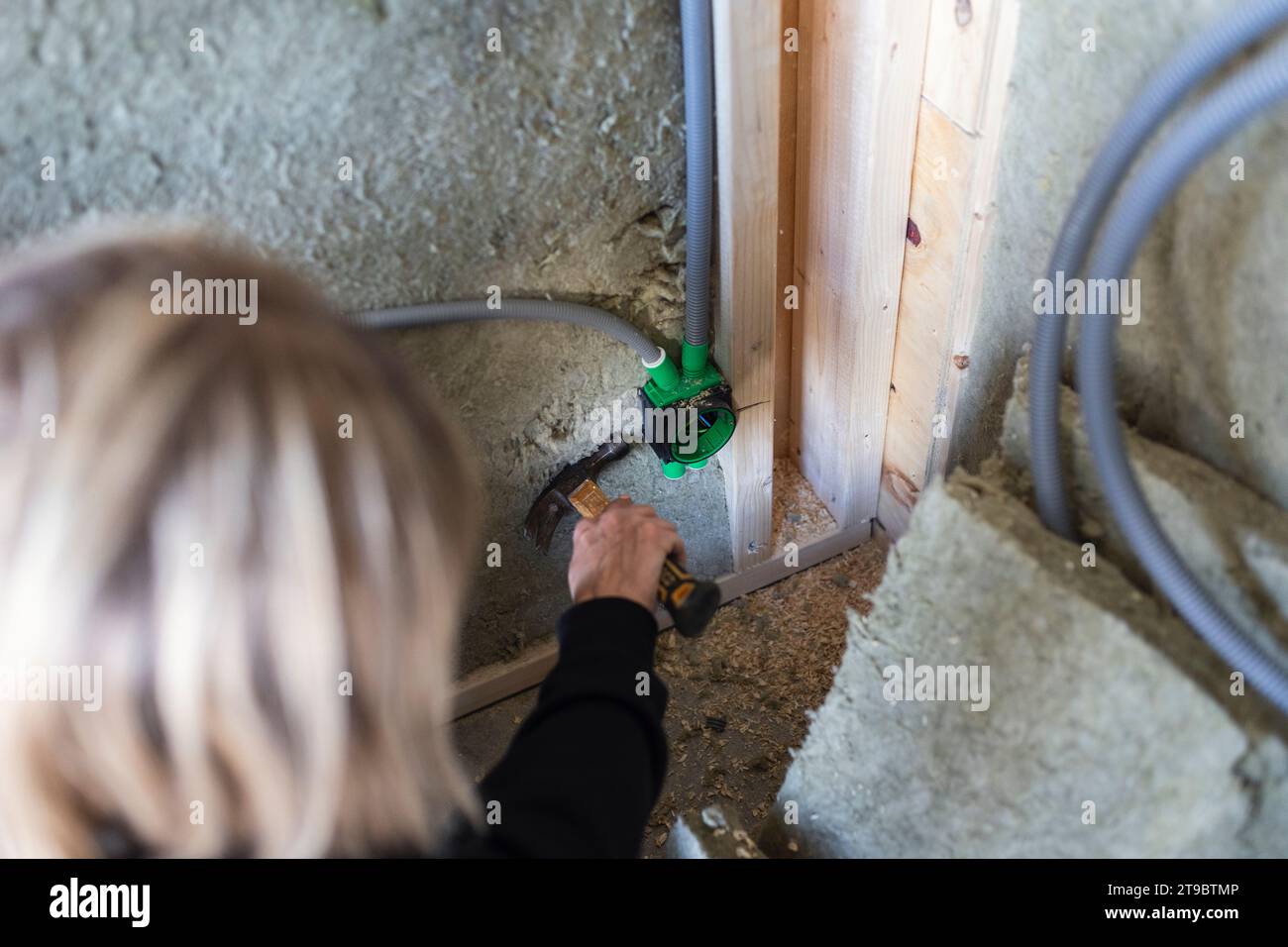 Female blue-collar worker working with hammer on wall Stock Photo