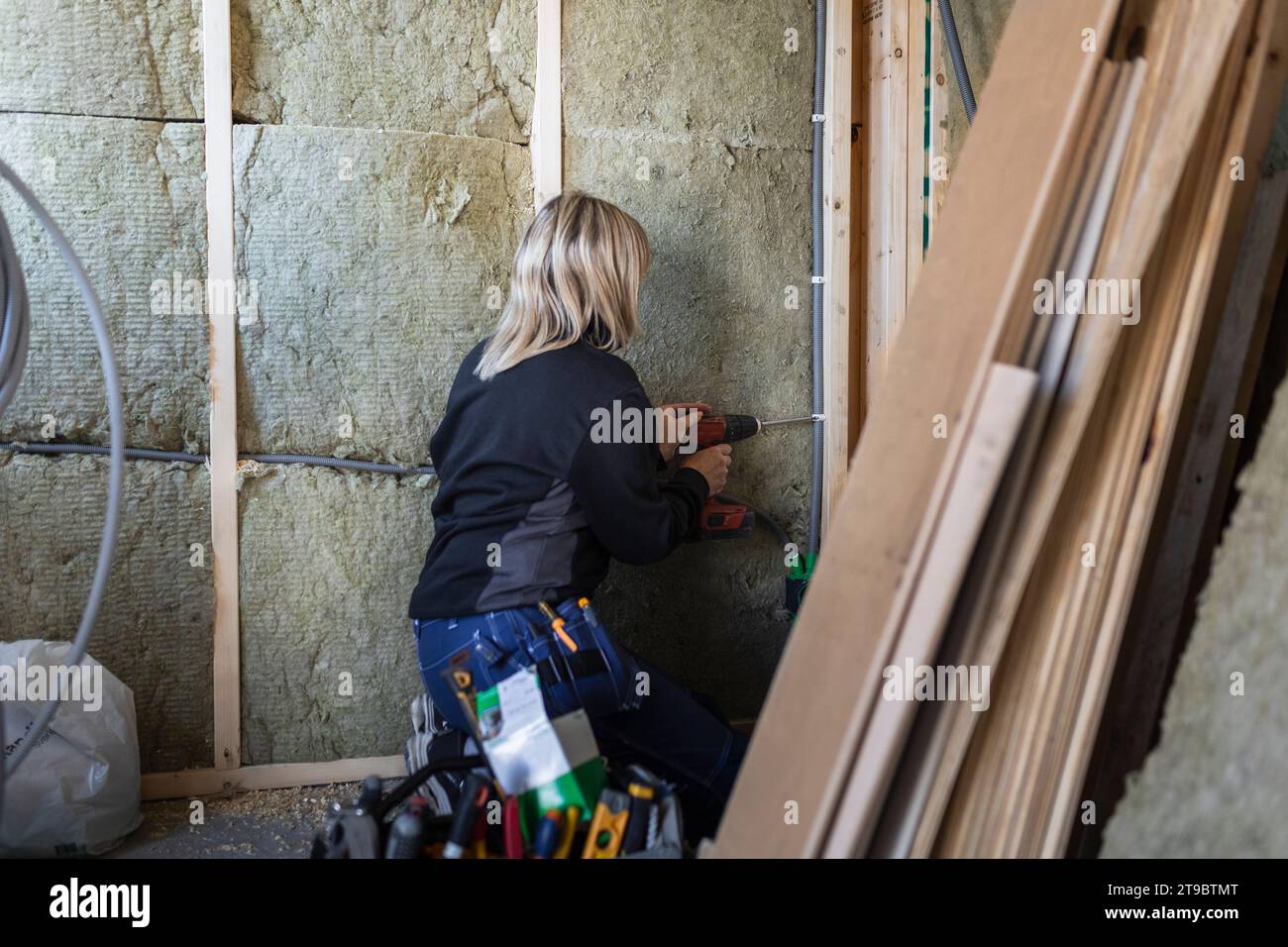 Blond female technician with drill machine drilling wall Stock Photo