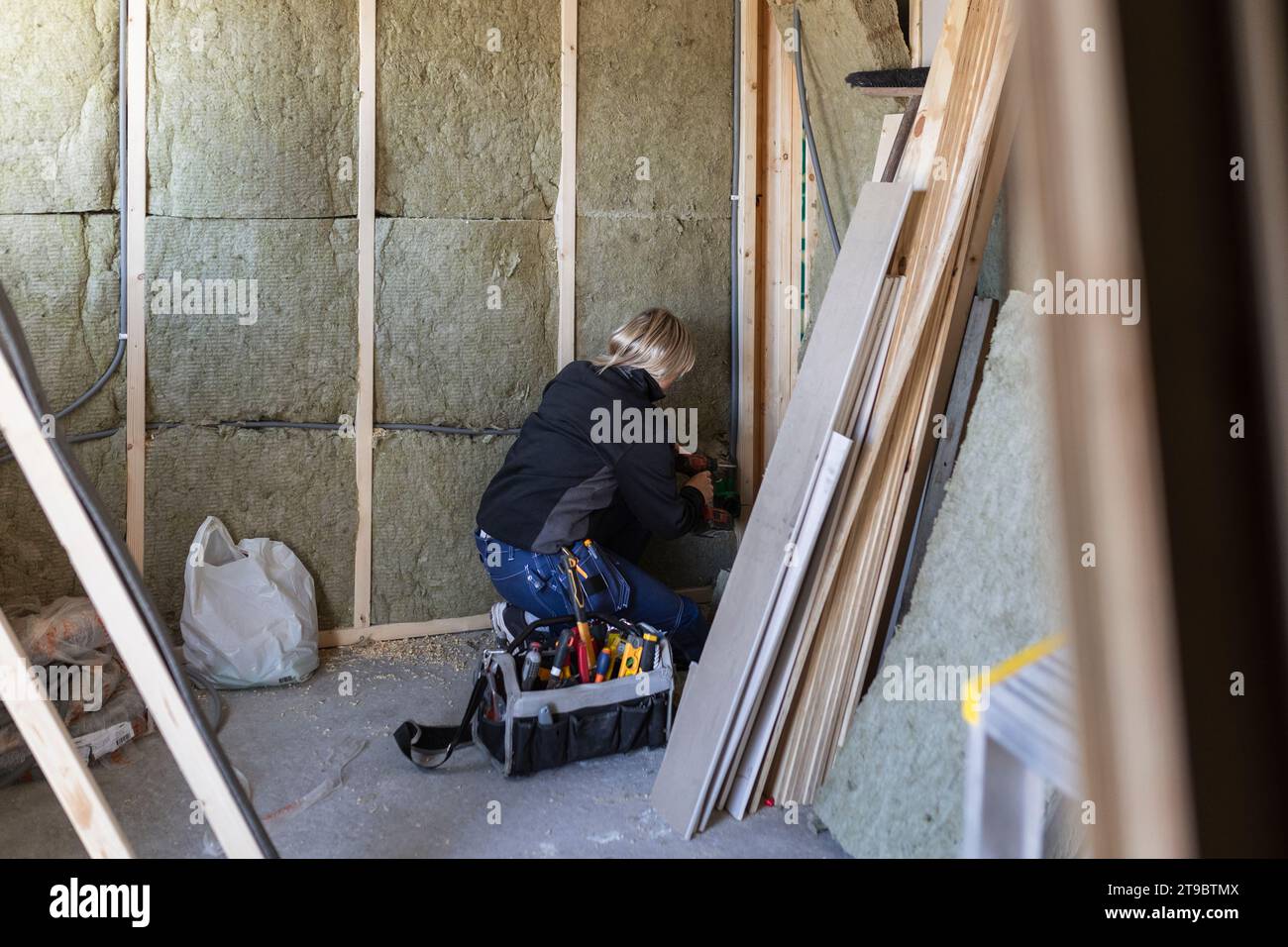 Female technician with drill machine drilling on wall by tool box Stock Photo