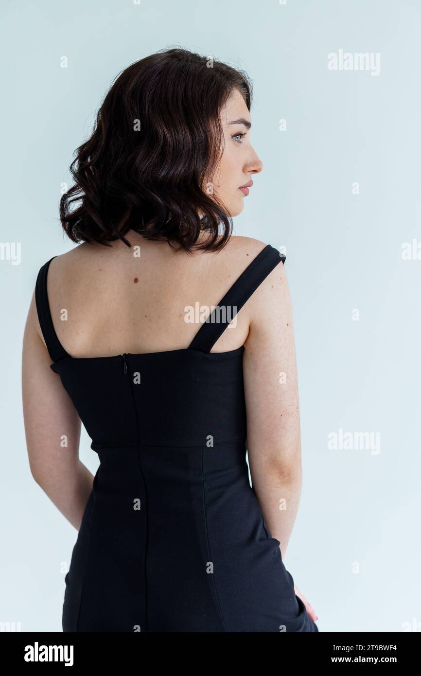 Portrait of a young beautiful girl in a black dress on a gray ...