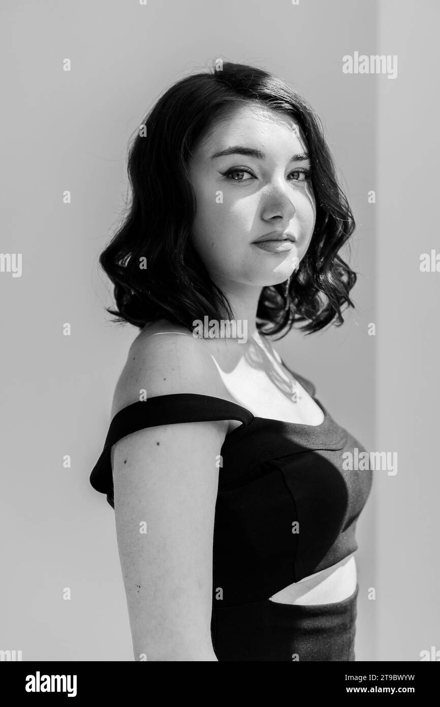 Portrait of a young beautiful girl in a black dress on a gray ...