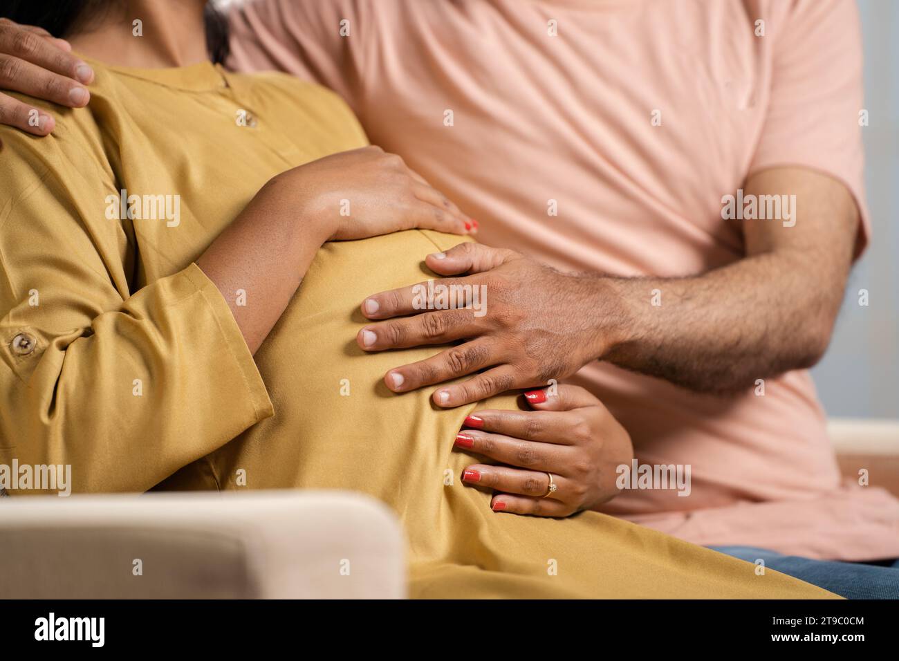 Close up shot of husband holding feeling by touching the belly of pregnant wife at home - concept of parenthood, affectionate and expecting. Stock Photo