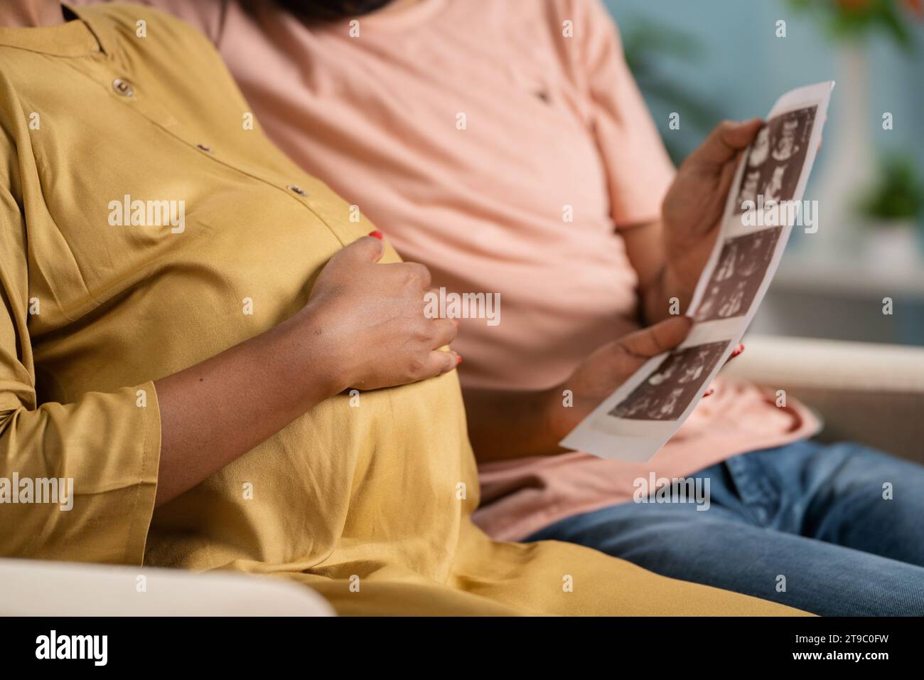 Close up shot of Indian pregnant woman with husband seeing baby ultrasound scan report at home - concept of parenthood, maternity and relationship Stock Photo