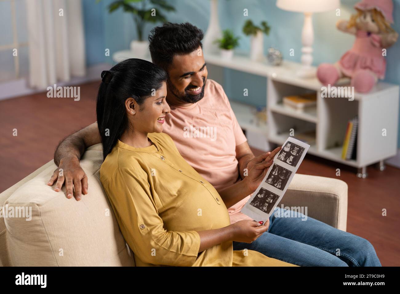 Happy Indian Pregnant women or wife with caring husband checking ultrasound scan reports at home - concept of Parenthood journey, bonding and Stock Photo