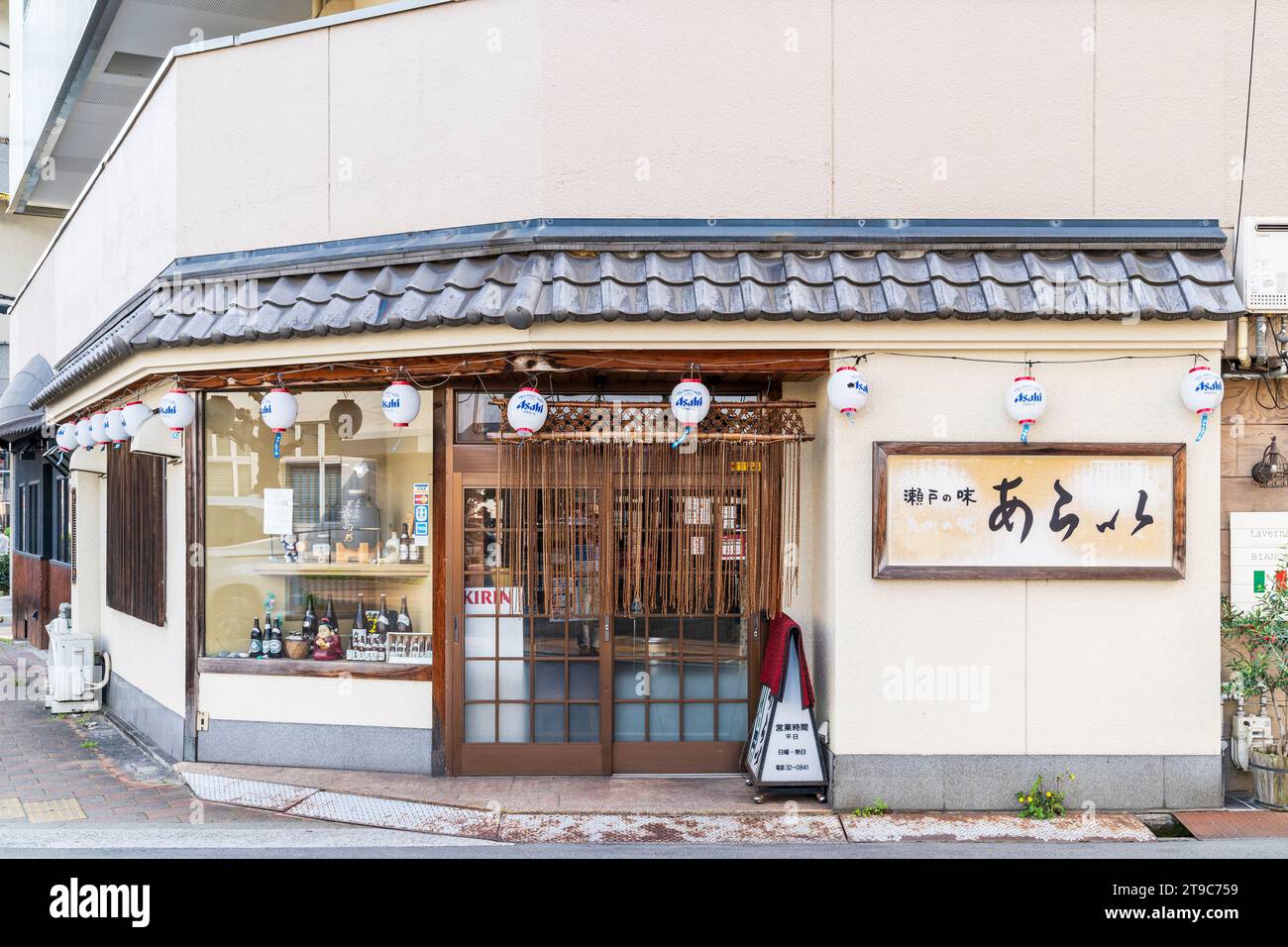 Exterior of Japanese restaurant in Fukuyama. Asahi lanterns hanging above the doorway and shuttered window. Modern facade. Daytime. Stock Photo