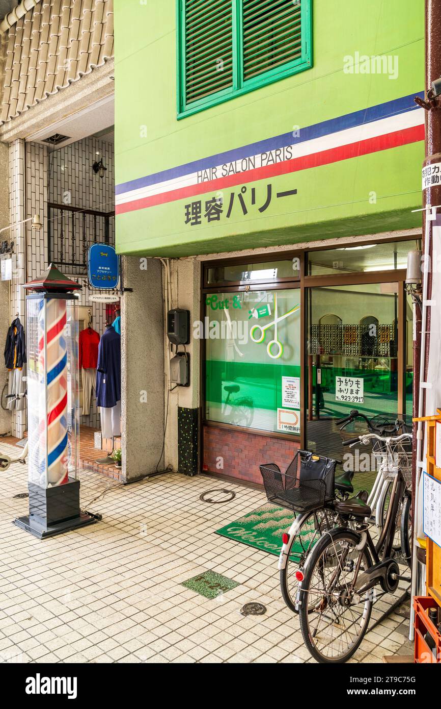 Downtown exterior of a Japanese hairdresser, 'Hair Salon Paris' with two bikes outside and typical barbers pole on the pavement. Stock Photo