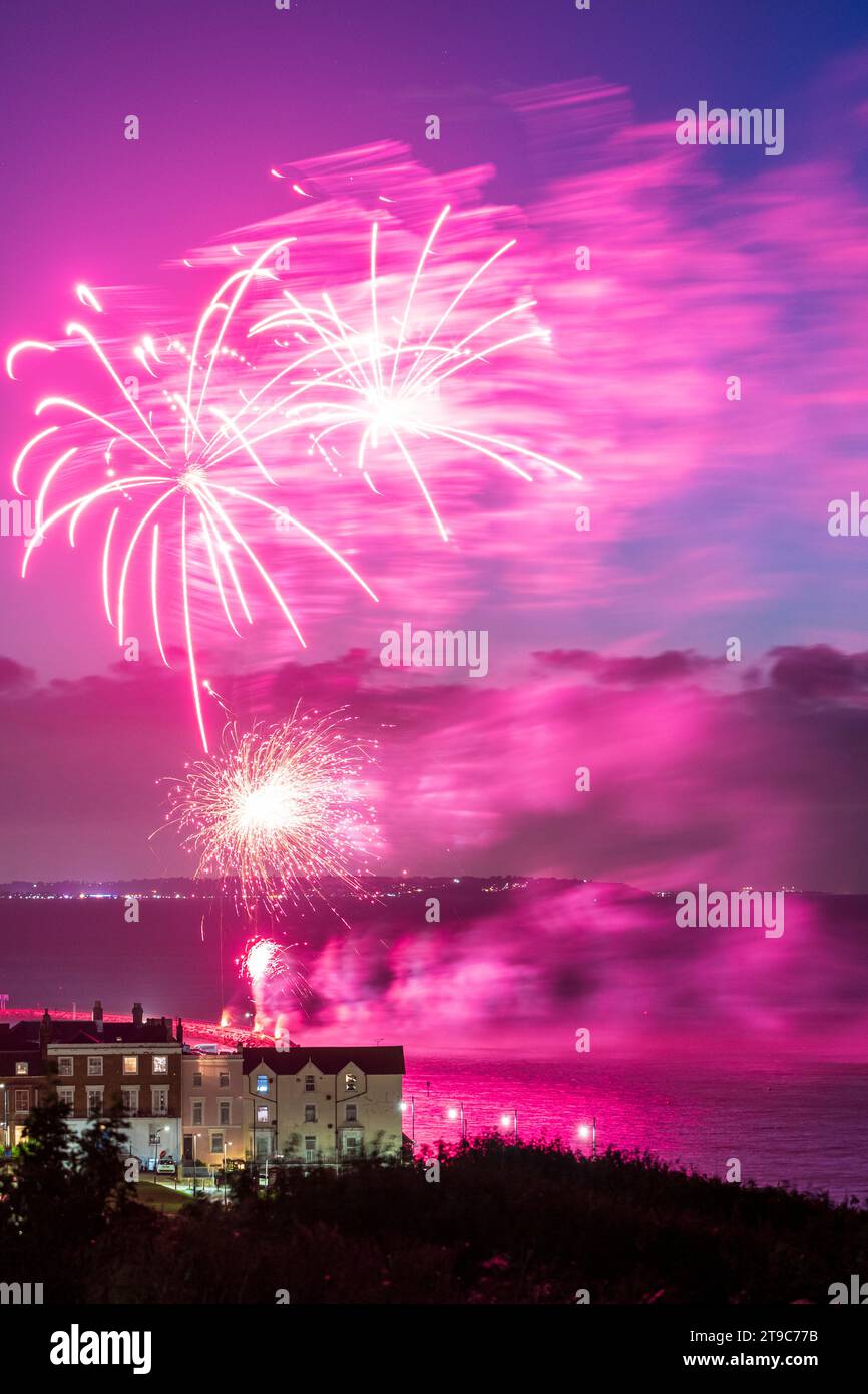 Fireworks bursting over the seafront and harbour at the Kent resort town of Herne Bay on a summer night. Isle of Sheppey in the background. Stock Photo