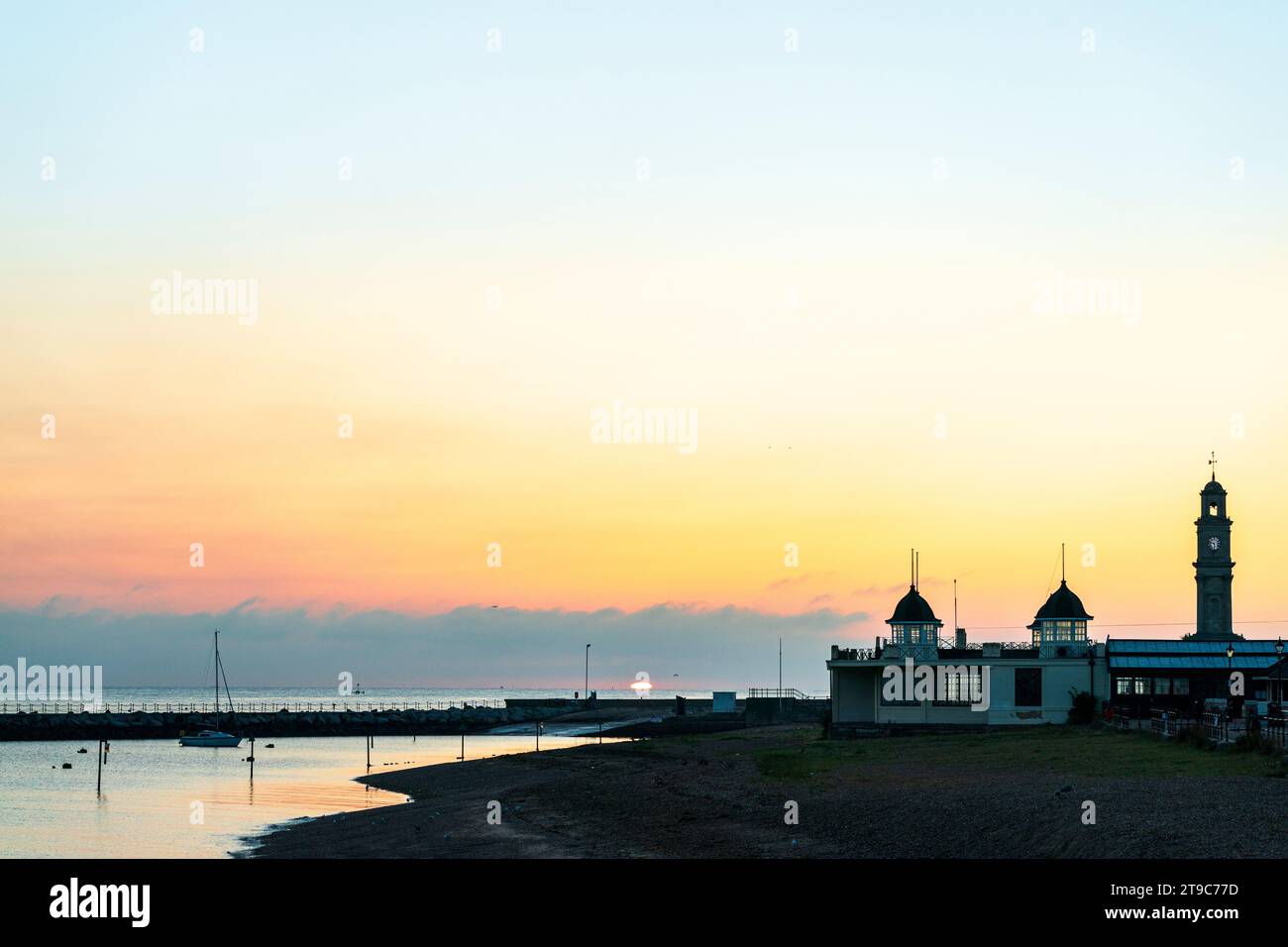 Sunrise over the seafront at Herne Bay with the Art Deco central bandstand, and the clock tower standing against the orange yellow sky. Stock Photo