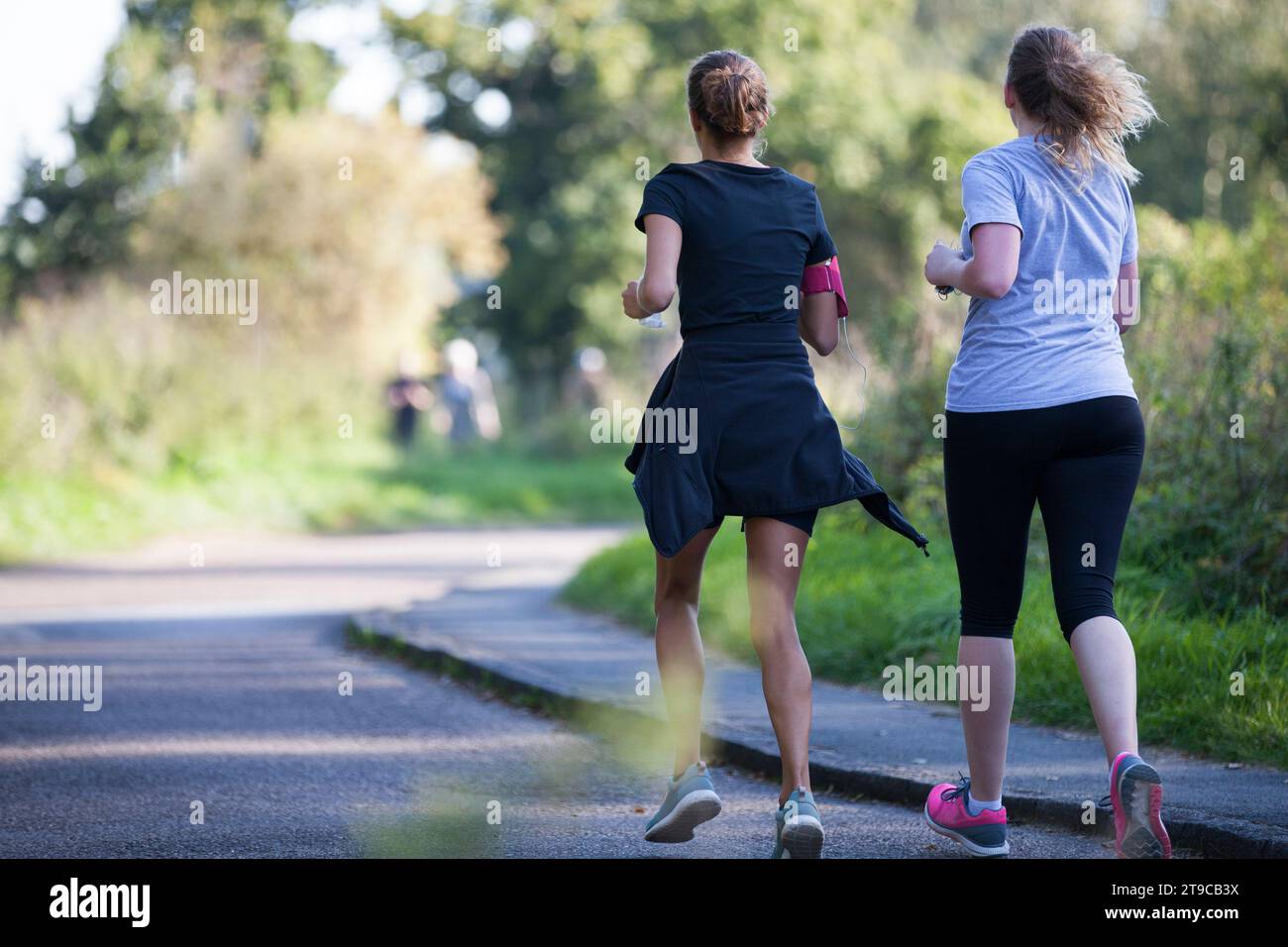 two female runners, jogging on a sunny day in leafy setting Stock Photo