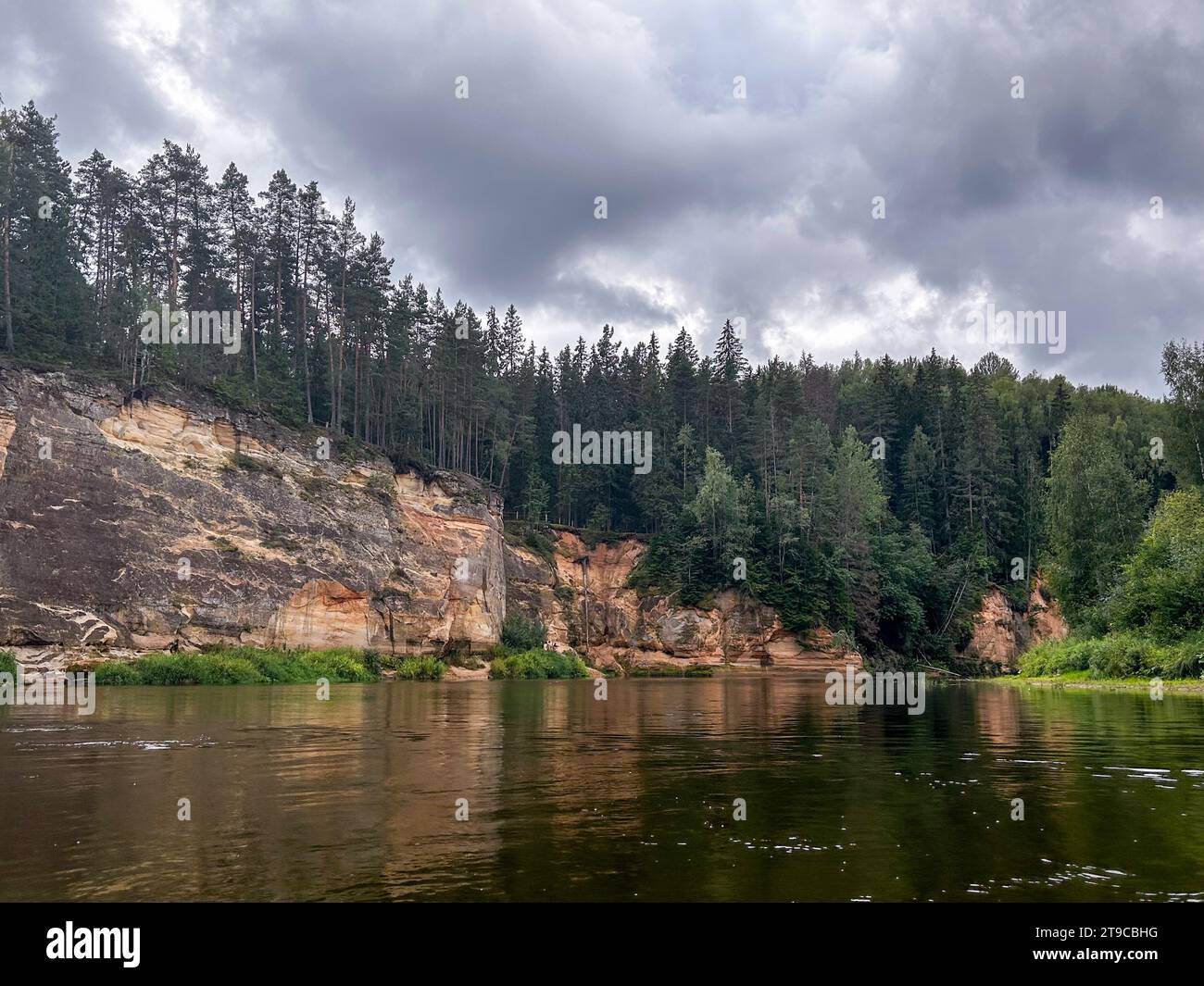Nature's Symphony: A tranquil river meanders gracefully, framed by the imposing beauty of cliffs and the serene embrace of lush woods, creating a harm Stock Photo