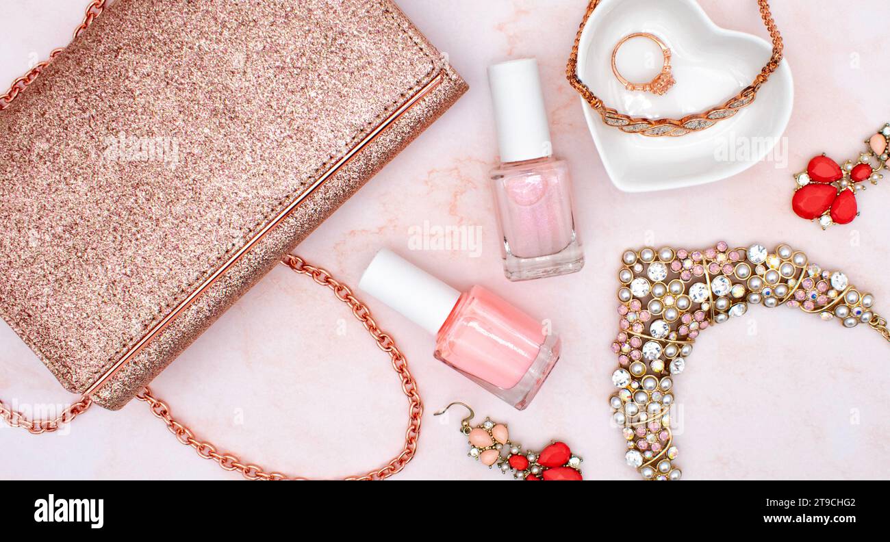 Rose gold flat lay fashion and jewelry concept with rose quartz background, pink nail polish, glitter clutch purse, and rose gold diamond jewelry Stock Photo