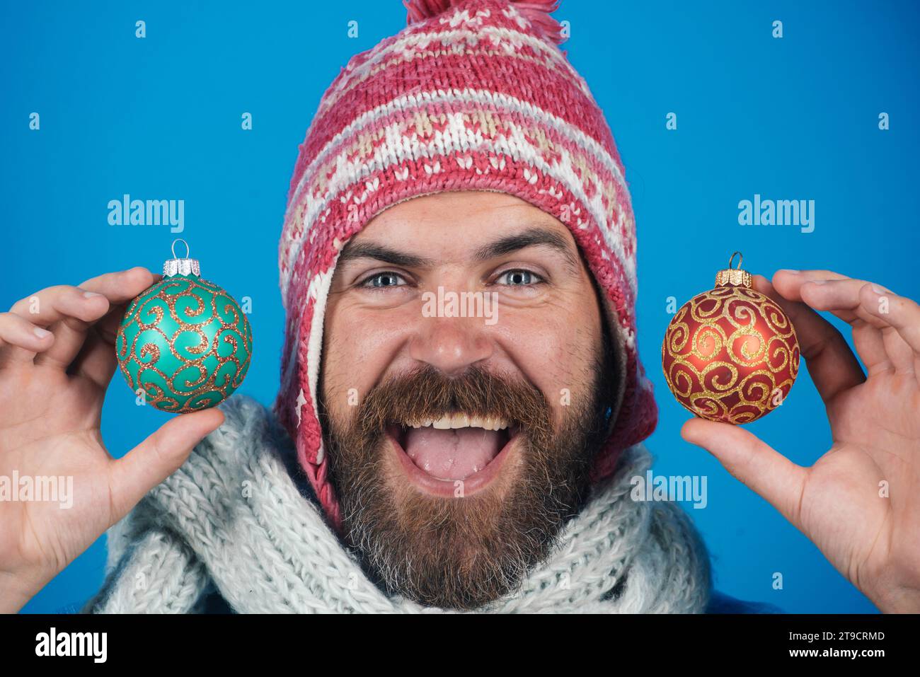 Happy man in winter wear with golden colored Christmas tree toys. Holiday decorations and ornaments. Christmas or New Year celebration. Bearded man Stock Photo