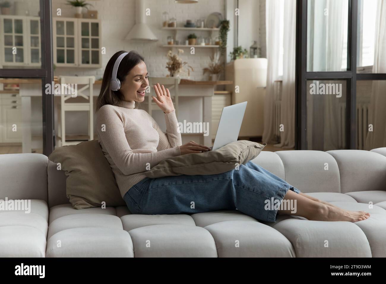 Woman wear headphones greets friend start videoconference use laptop Stock Photo