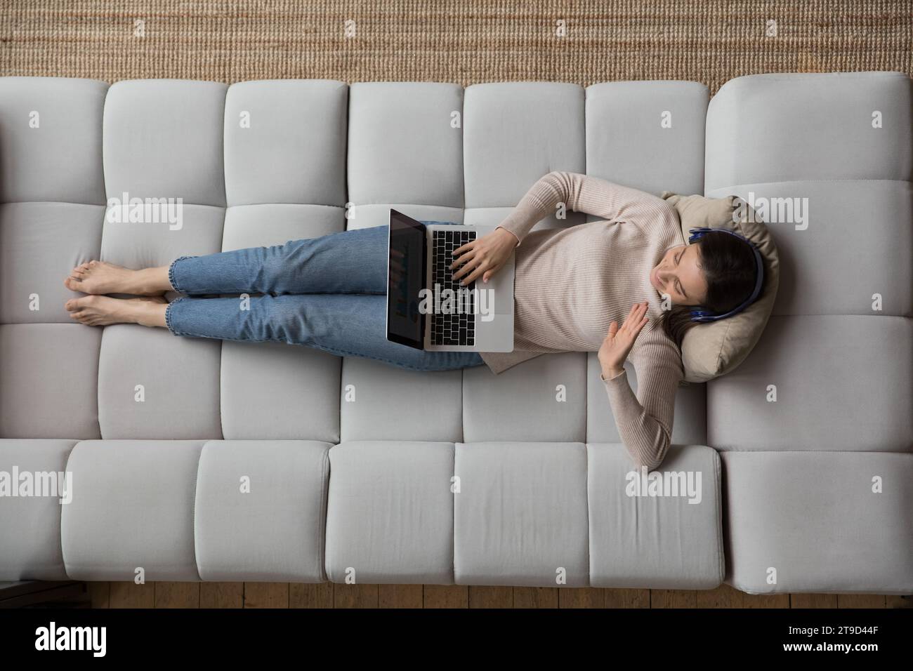 Woman lying on couch with laptop, greeting friend start videocall Stock Photo